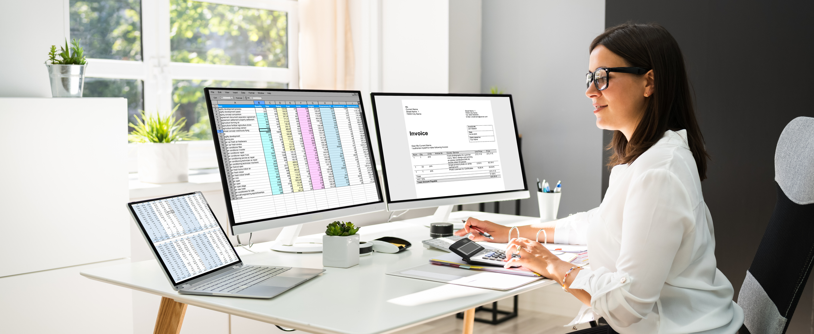 A woman looking at spreadsheets on multiple computer screens while entering numbers into a calculator.