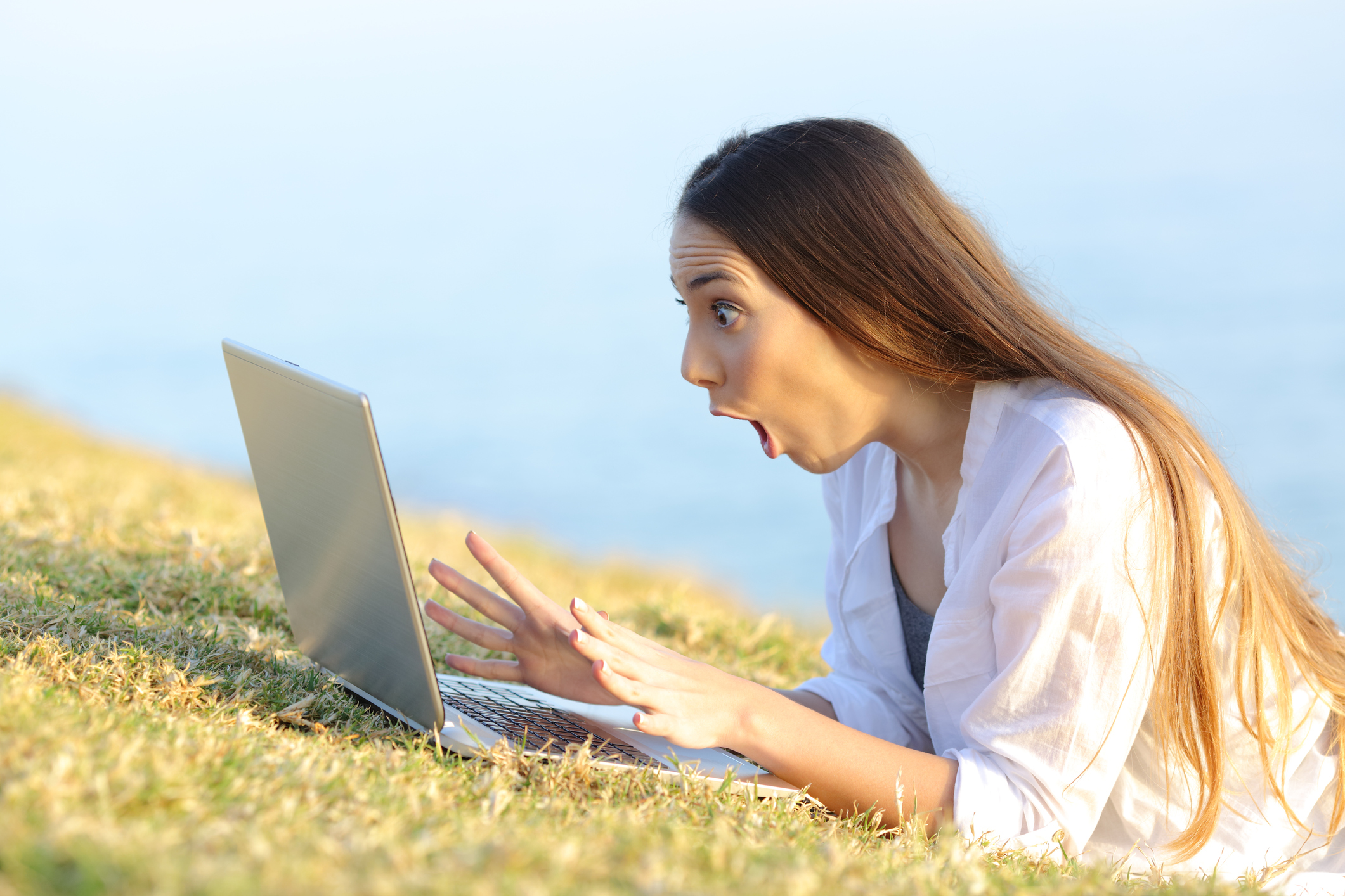 A young woman gasps in shock at her laptop computer.