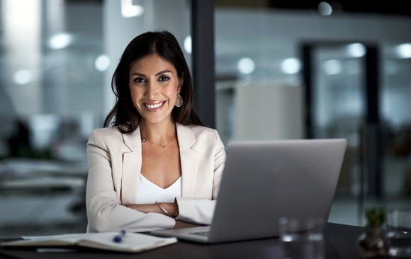 Smiling professionally dressed person at a laptop.