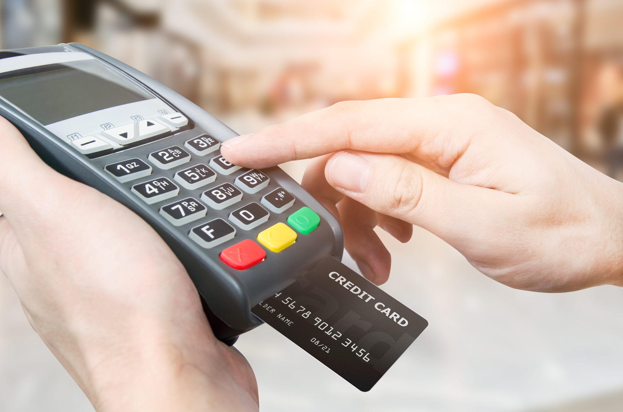 Hands holding mobile point of sale device with credit card entering a code.