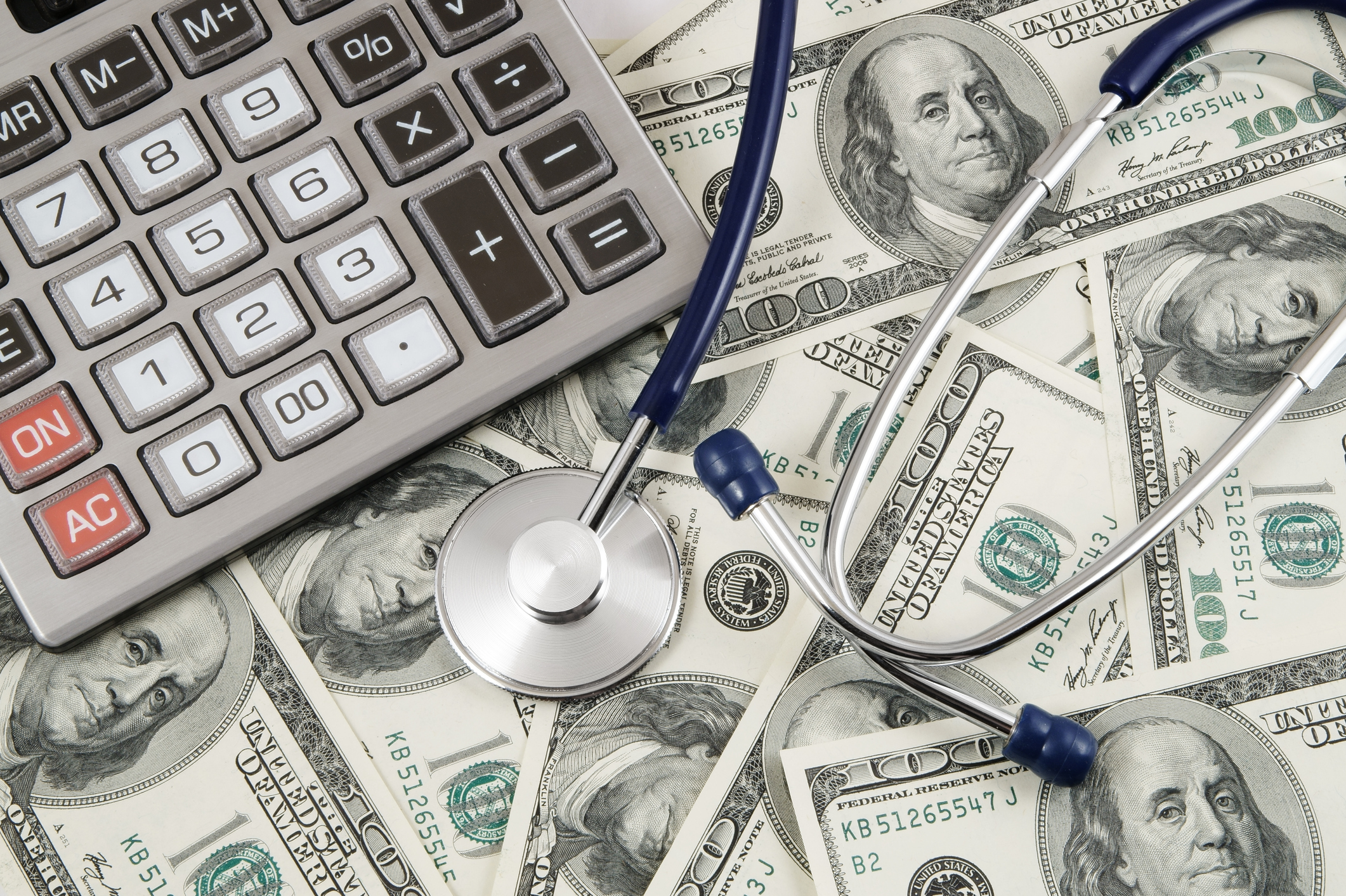 Cash spread across a surface with a stethoscope and calculator on top.