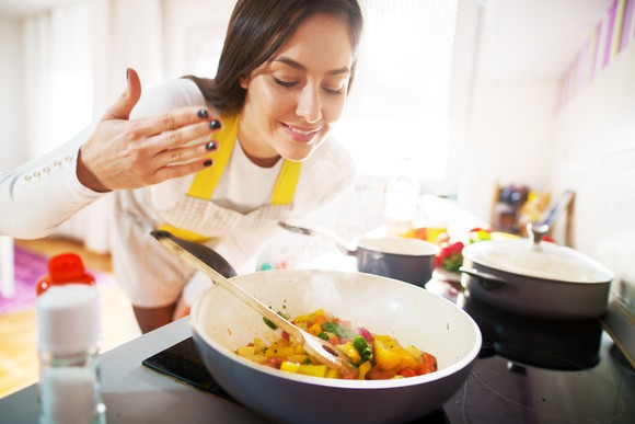 Home cook enjoying the aromas wafting up from a bowl of cooked vegetables on the stove. 