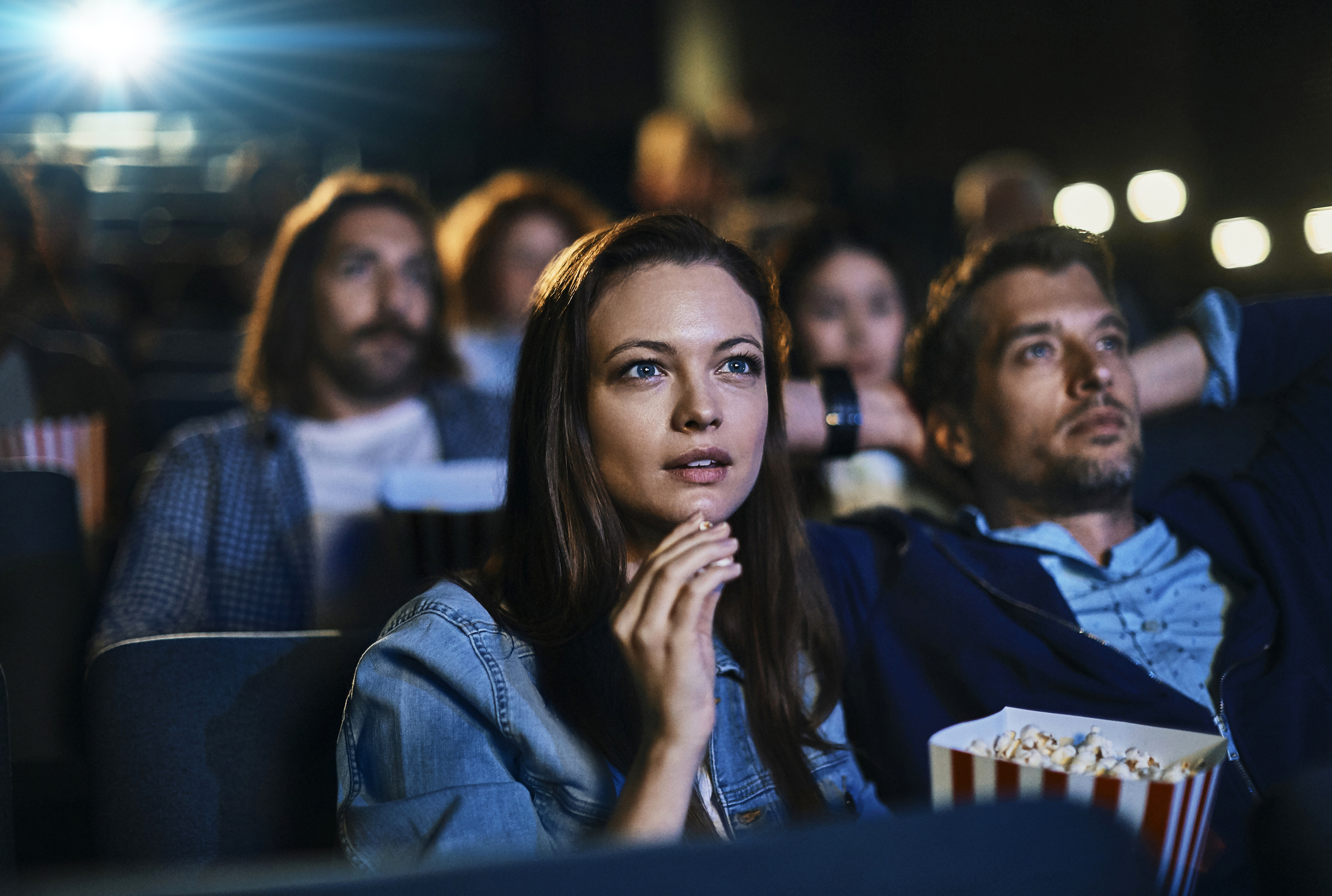 A couple eating popcorn while watching a movie in a crowded theater.