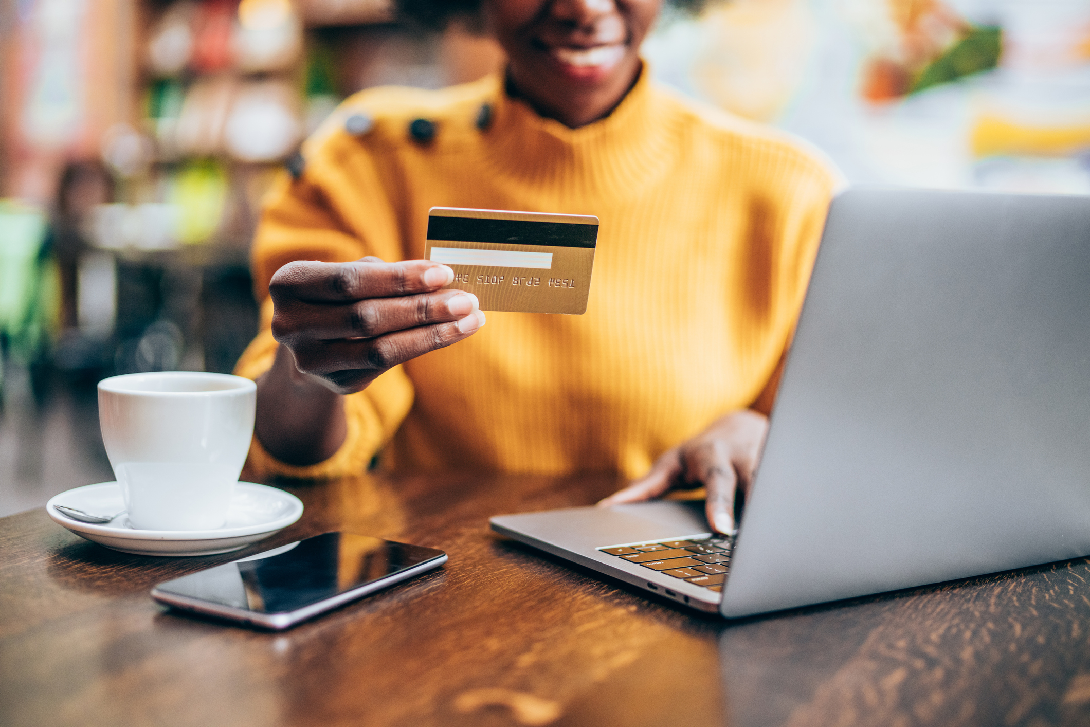 A woman holding up a credit card in her left hand while typing on a laptop with her right.