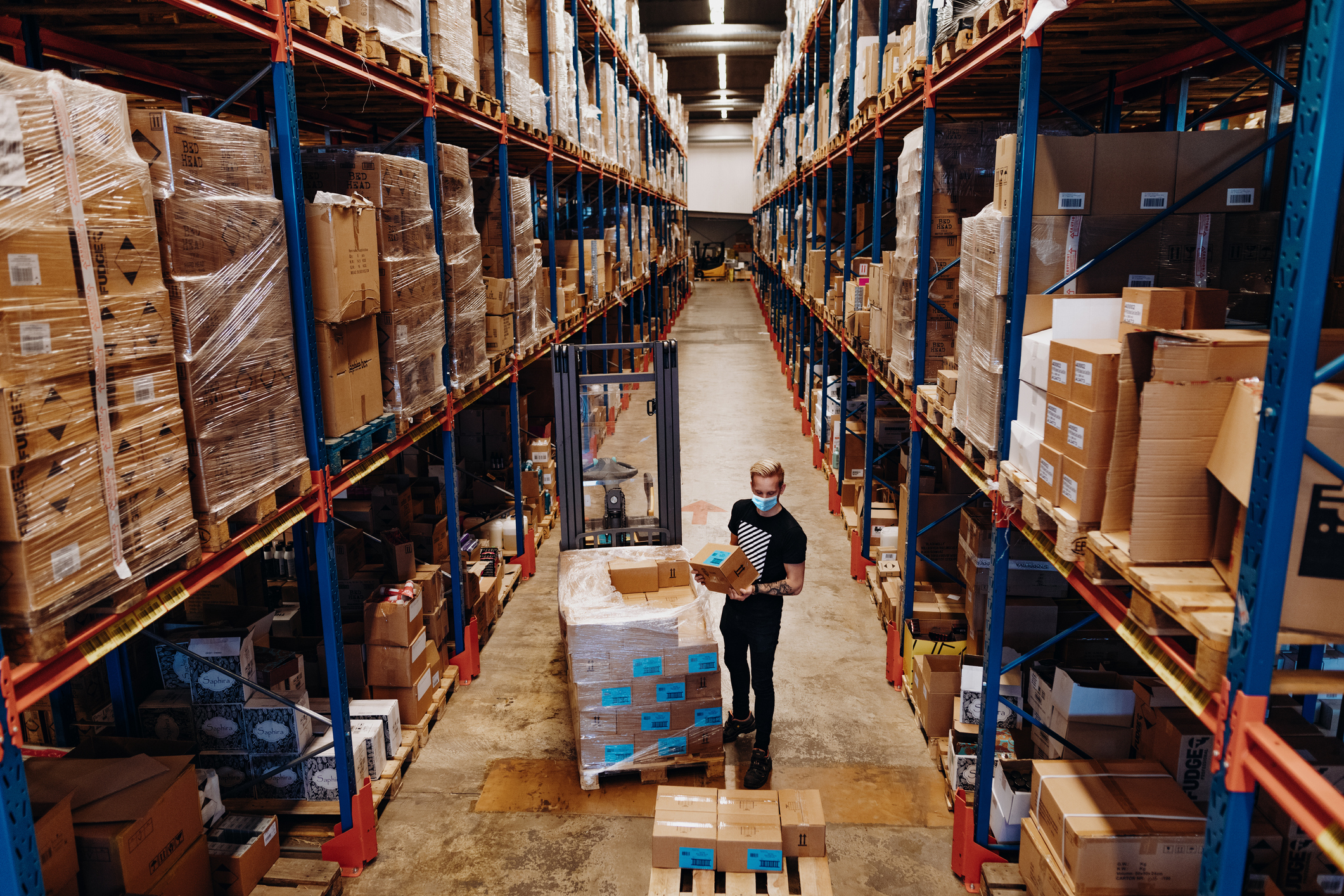 A warehouse employee wearing a face mask unloads parcels.