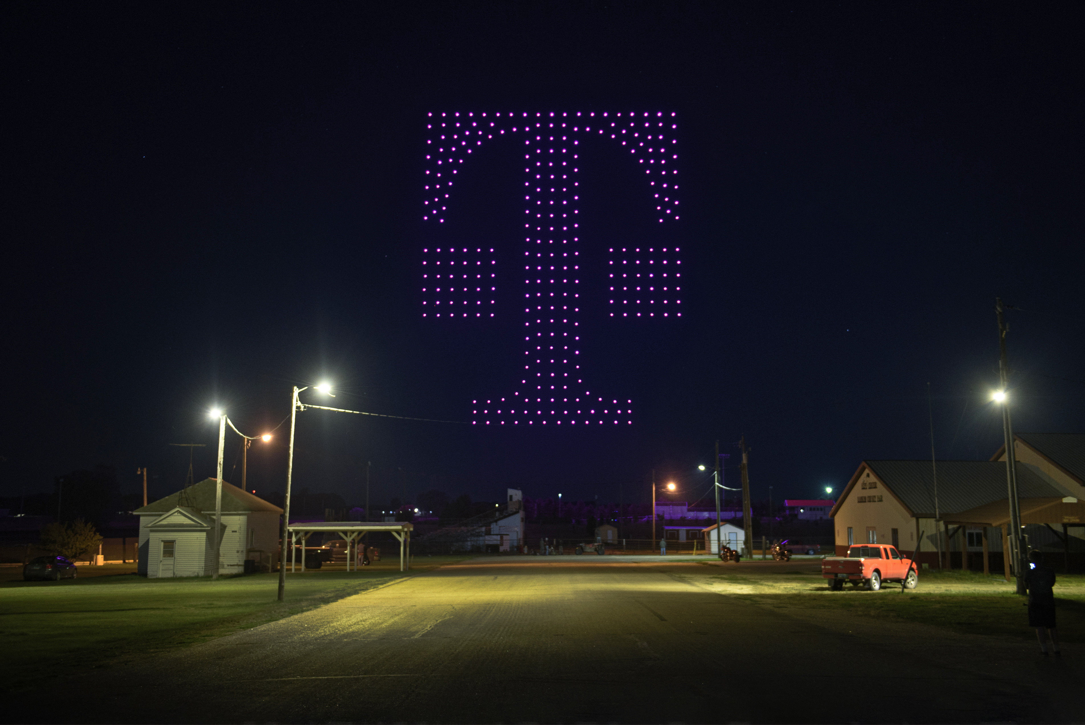 Drones with magenta lights forming the T-Mobile logo in the night sky.