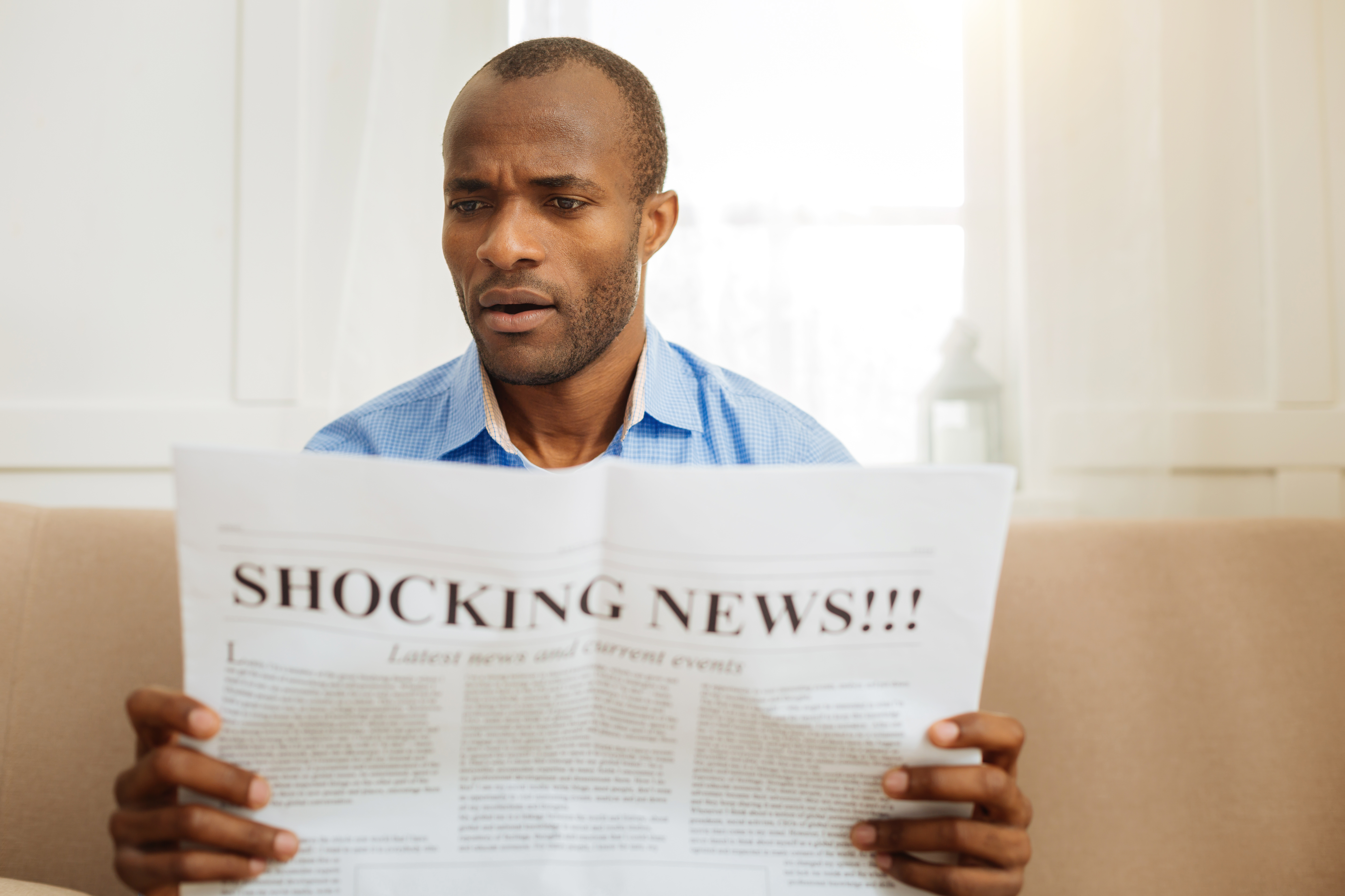A man reads a newspaper with a front page headline of shocking news.