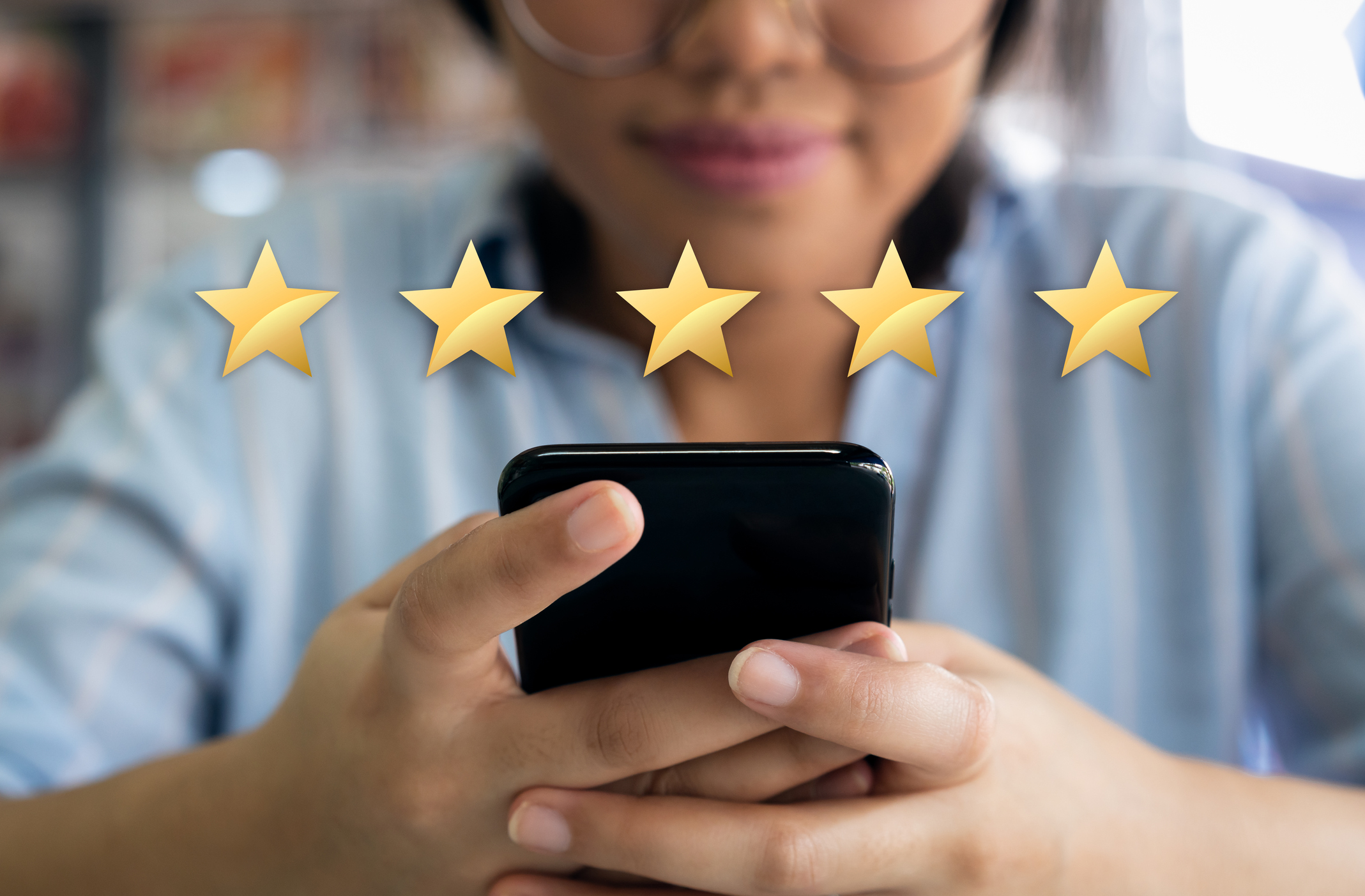 A young woman using a smartphone. Five gold stars hover in the air over the phone.