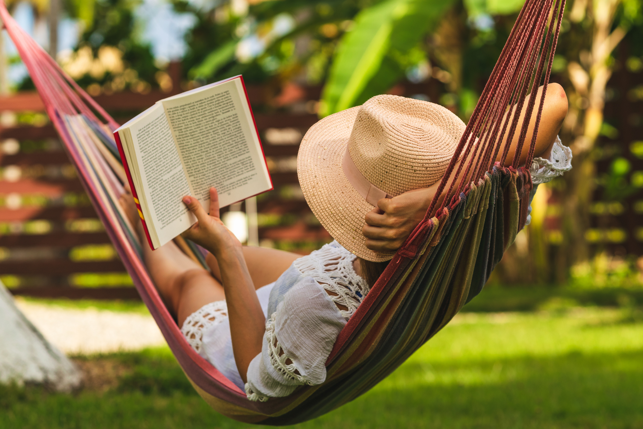 A person reading a book while lying in a hammock.
