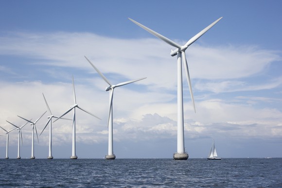 A sailboat drifts past offshore wind turbines. 
