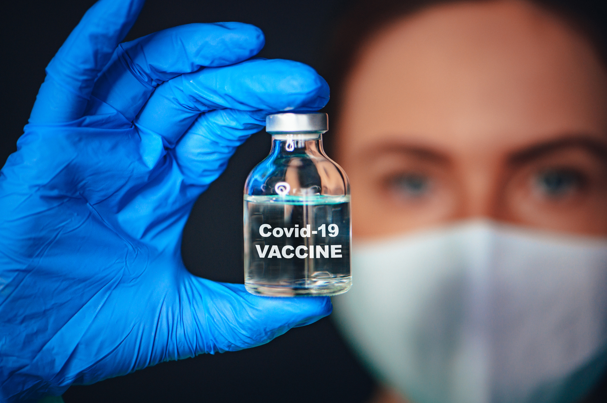 Nurse holding glass vial labeled "Covid-19 vaccine."