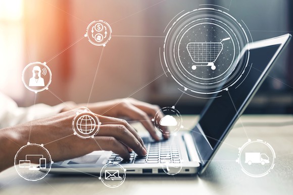 Hands typing on laptop with different digital icons around it.