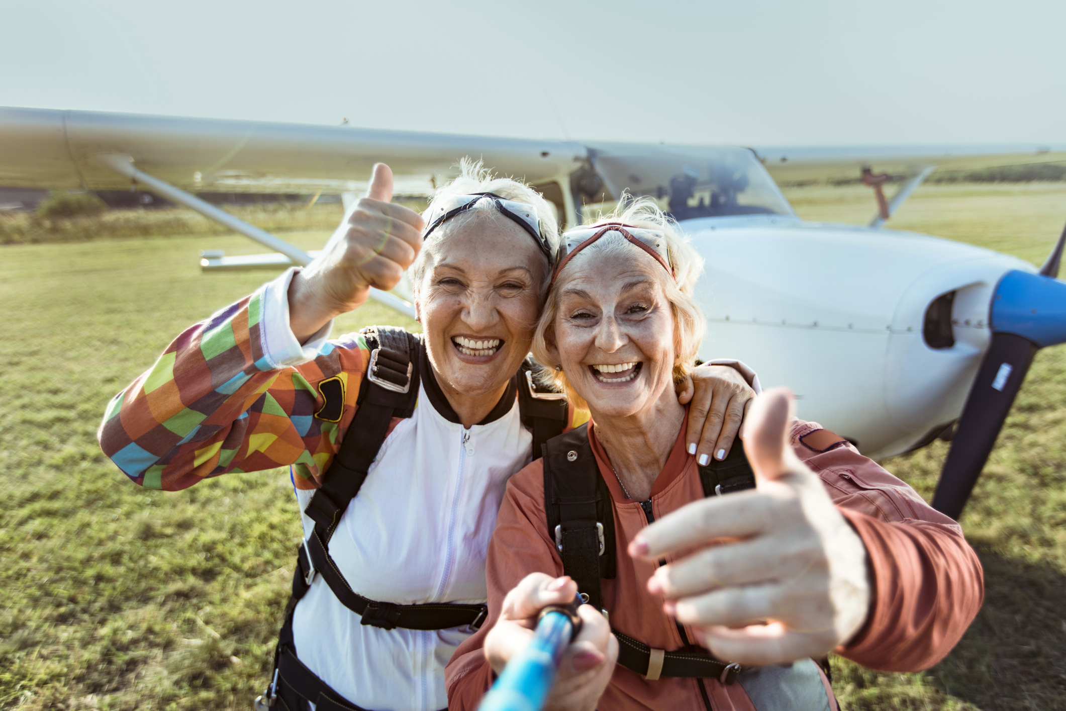 We see two happy senior women with thumbs up next to a propeller plane.