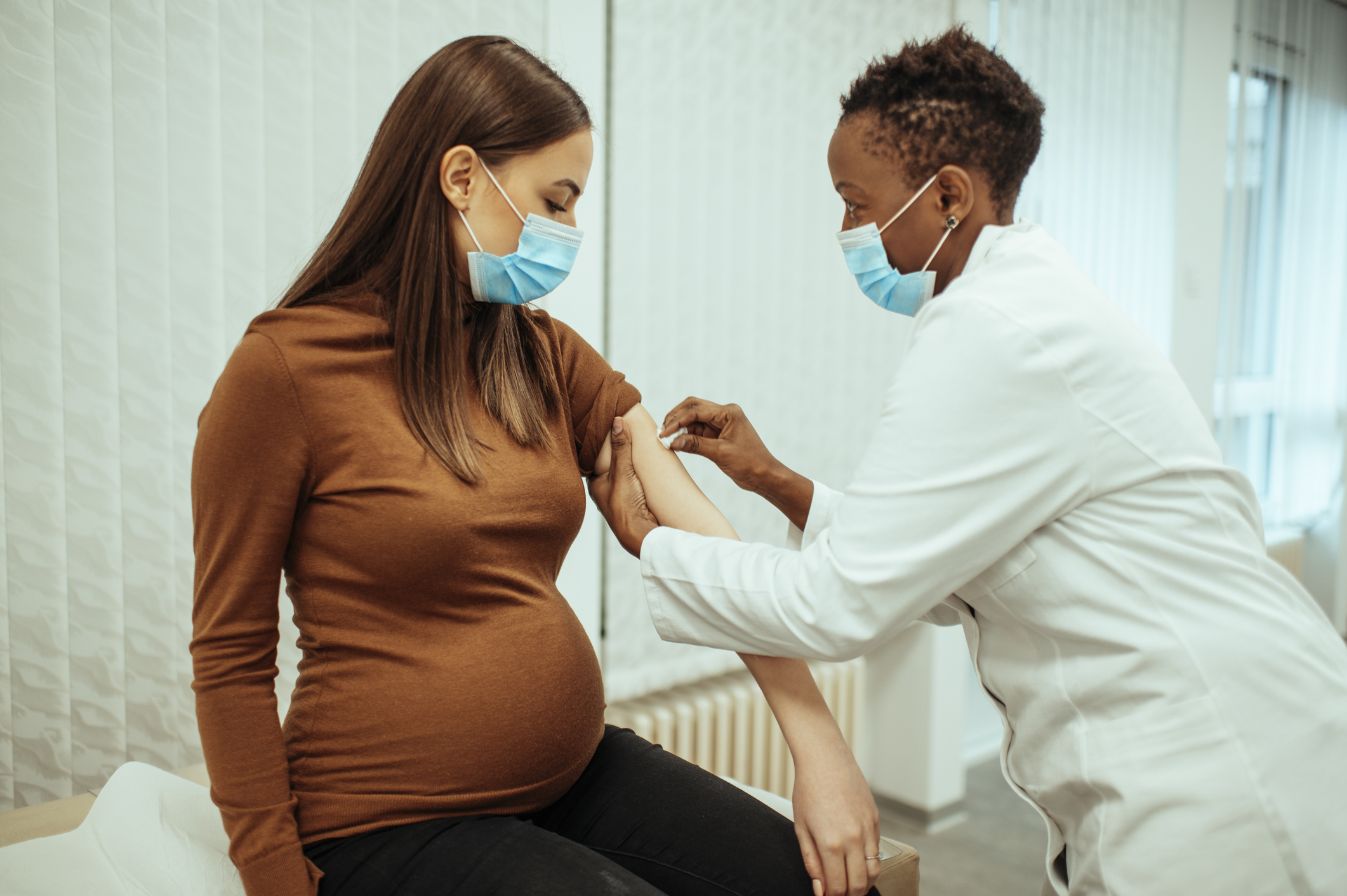 Pregnant woman receiving an injection from a medical professional.