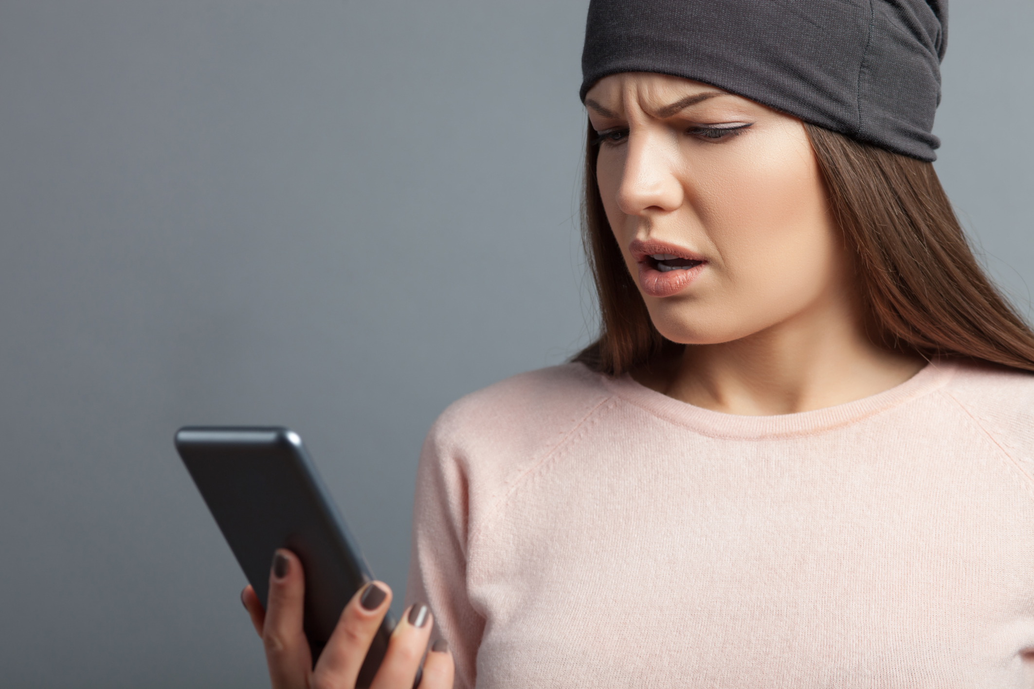 A young woman squints at her smartphone.