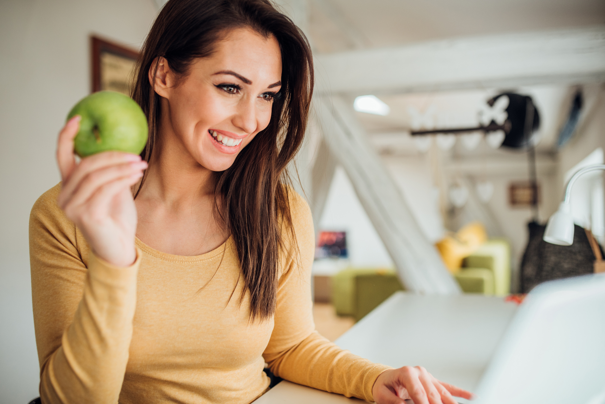 Woman holding an apple when using laptop.
