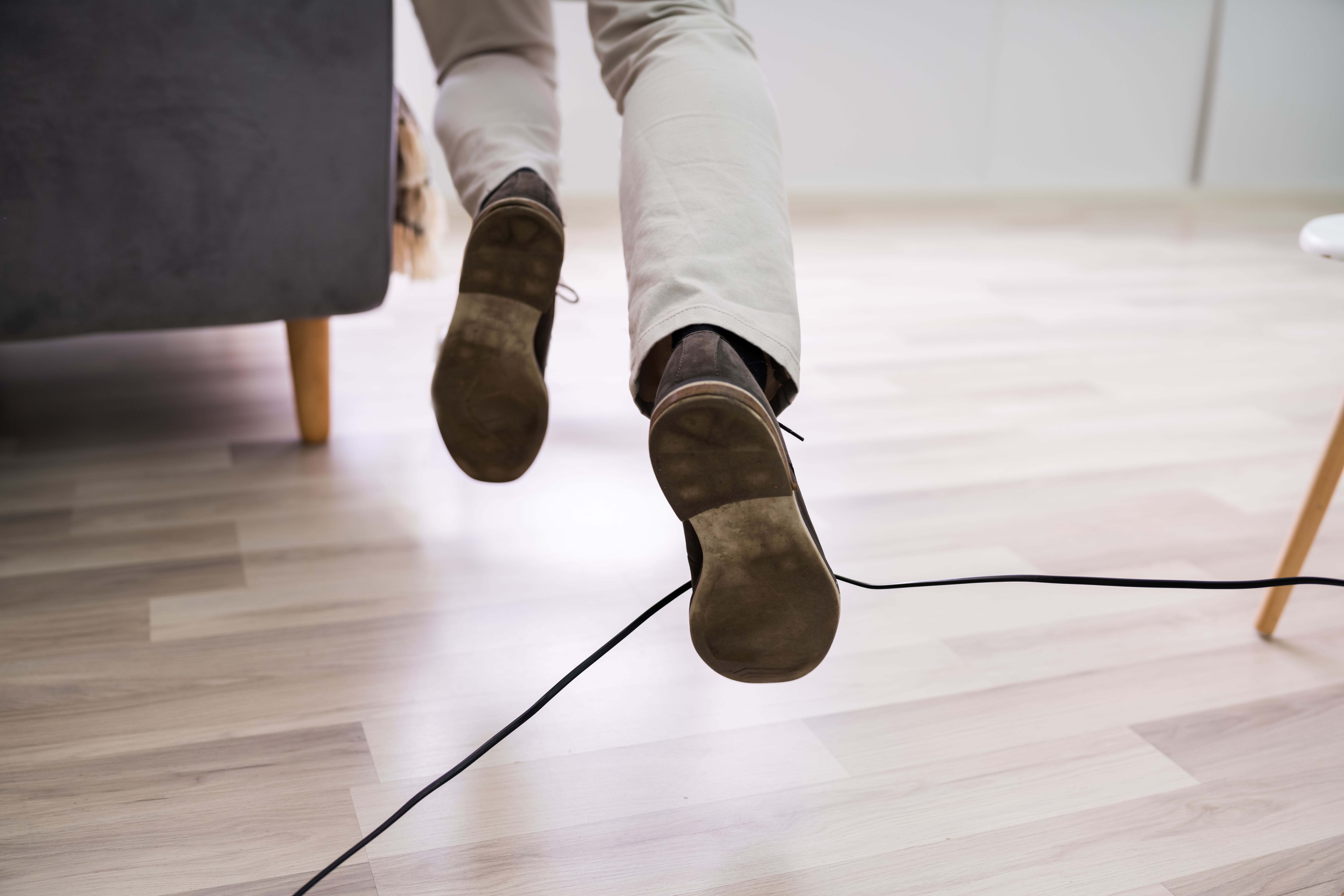 A person's feet and legs are shown. The person is tripping over a cord.