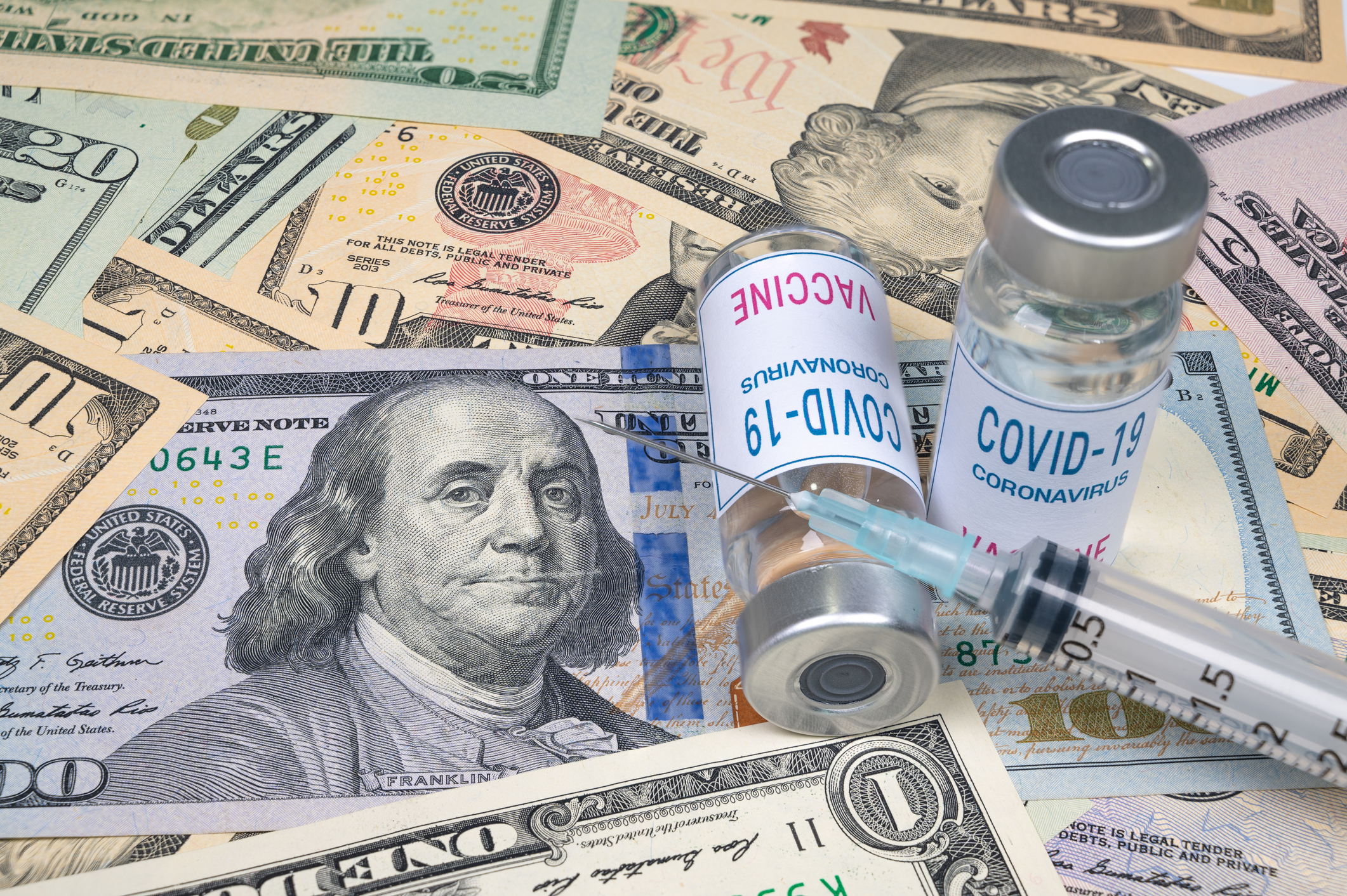 COVID-19 vaccine vials and syringe on top of cash
