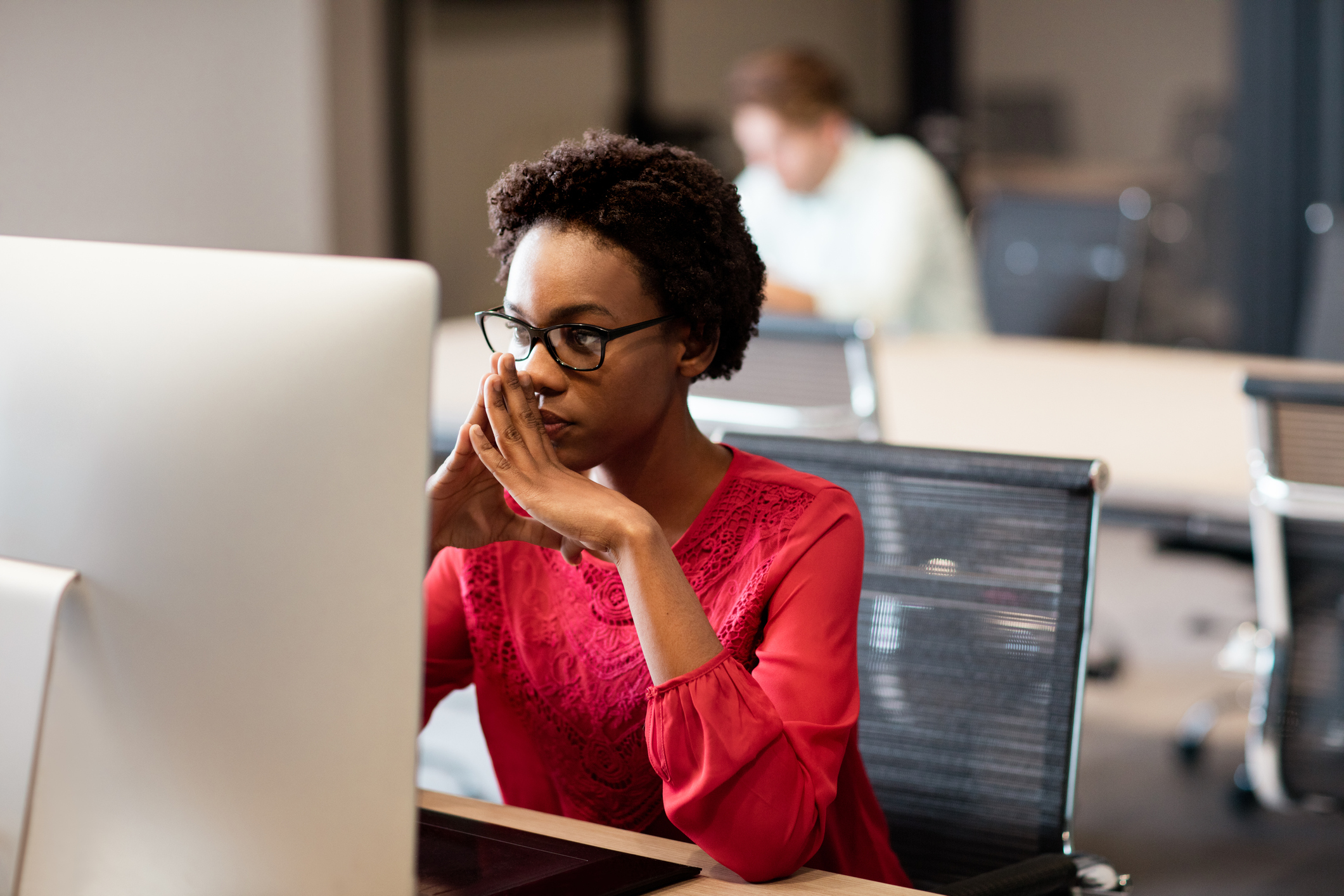 A woman sits pensively in front of a computer monitor.