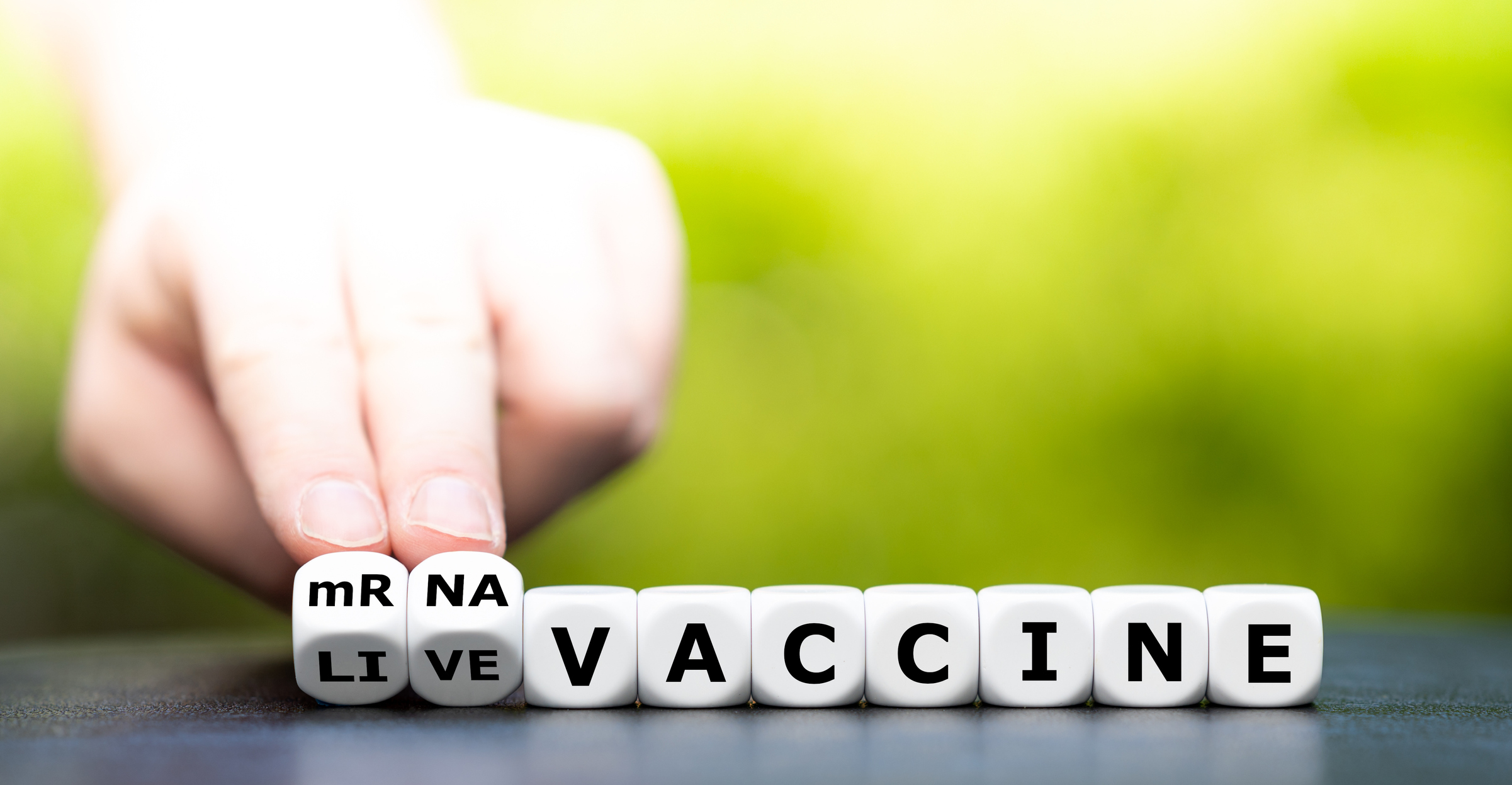 Dice with mRNA Vaccine spelled out and two fingers pushing the "mR" and "NA" dice to show the letters.