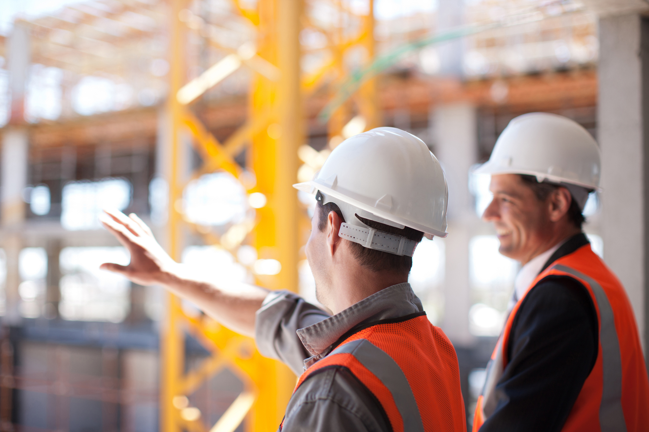 Two people wearing hard hats and reflective vests surveying a construction site