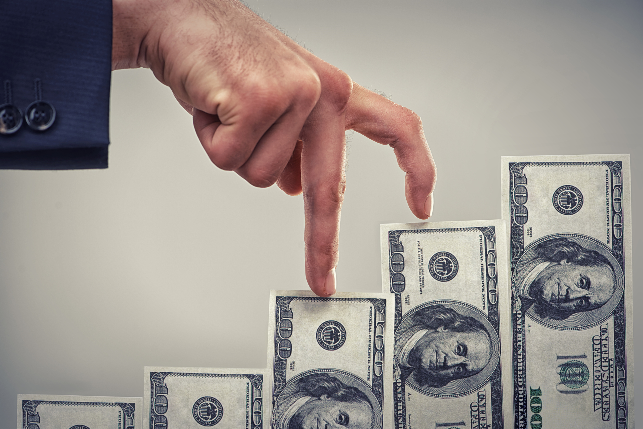 A man walking his fingers up a staircase of hundred dollar bills.