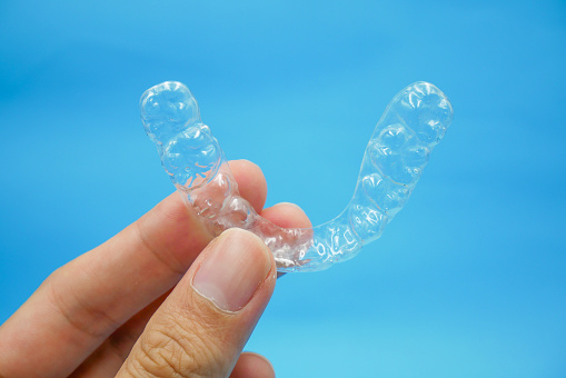 Hand holding up a clear teeth aligner.