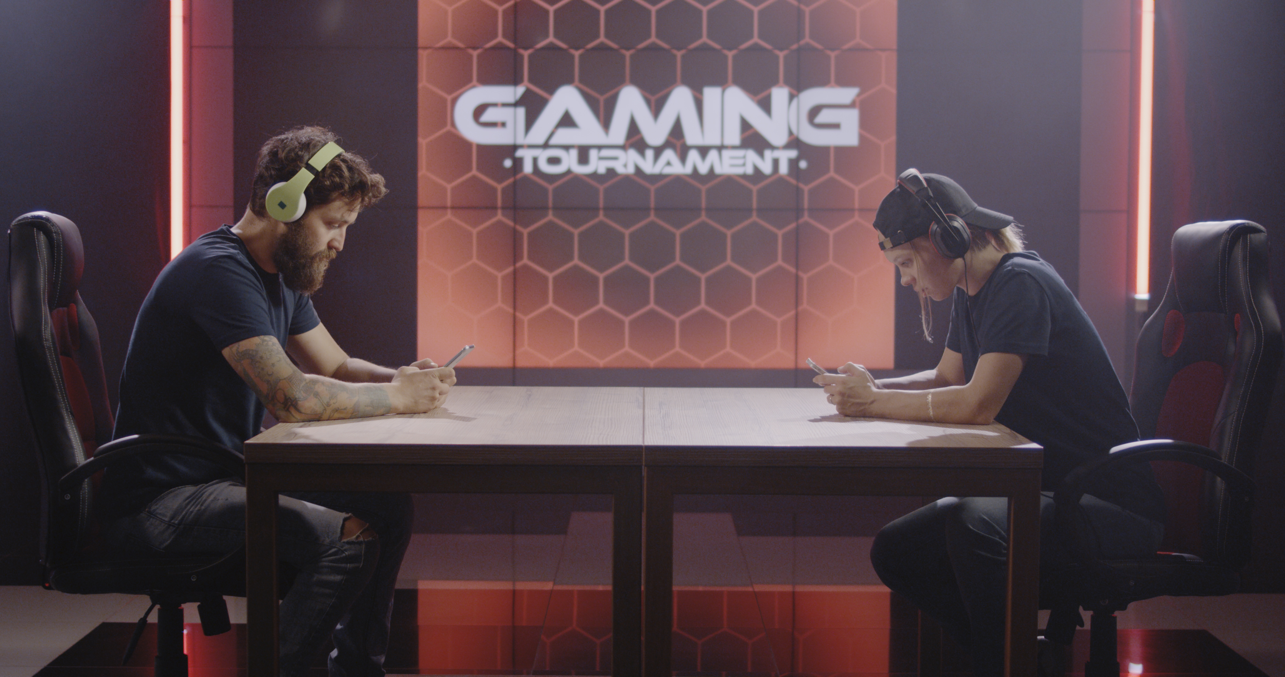 A man and a woman sitting at a table playing on their mobile devices in a gaming tournament.