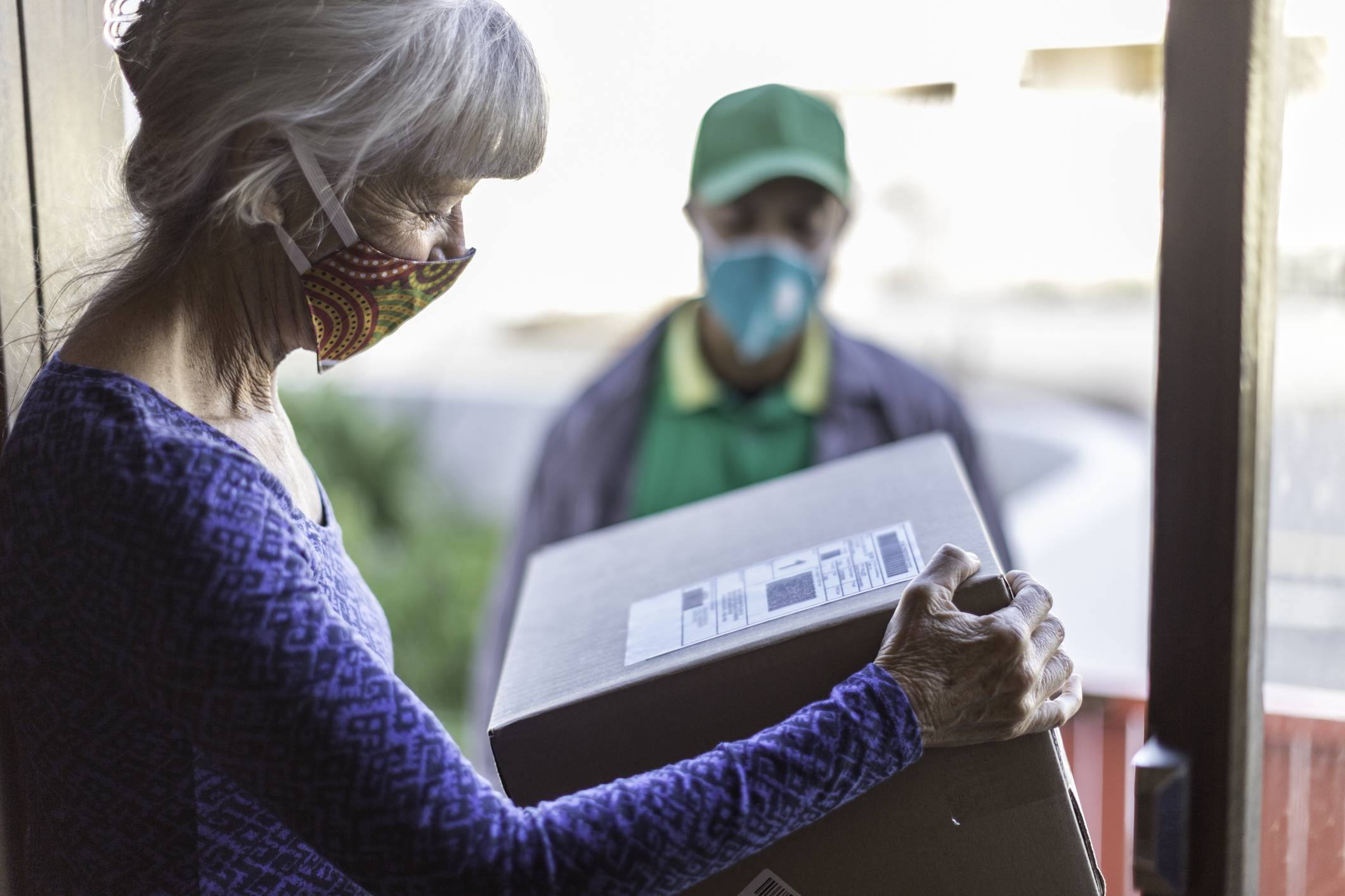 A senior woman looks at a package just delivered to her in her doorway.