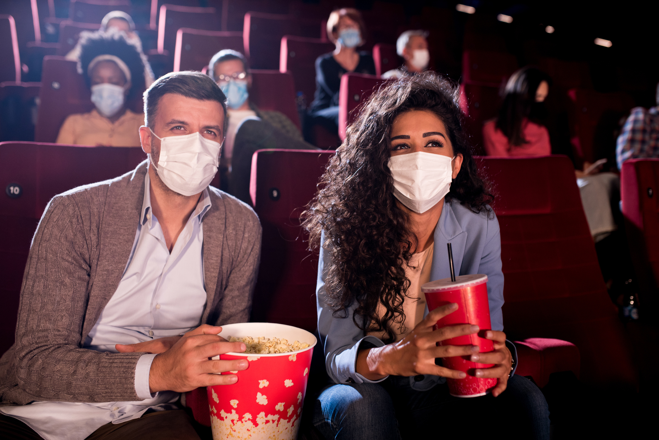 Two people wearing masks and holding popcorn at a movie theater.