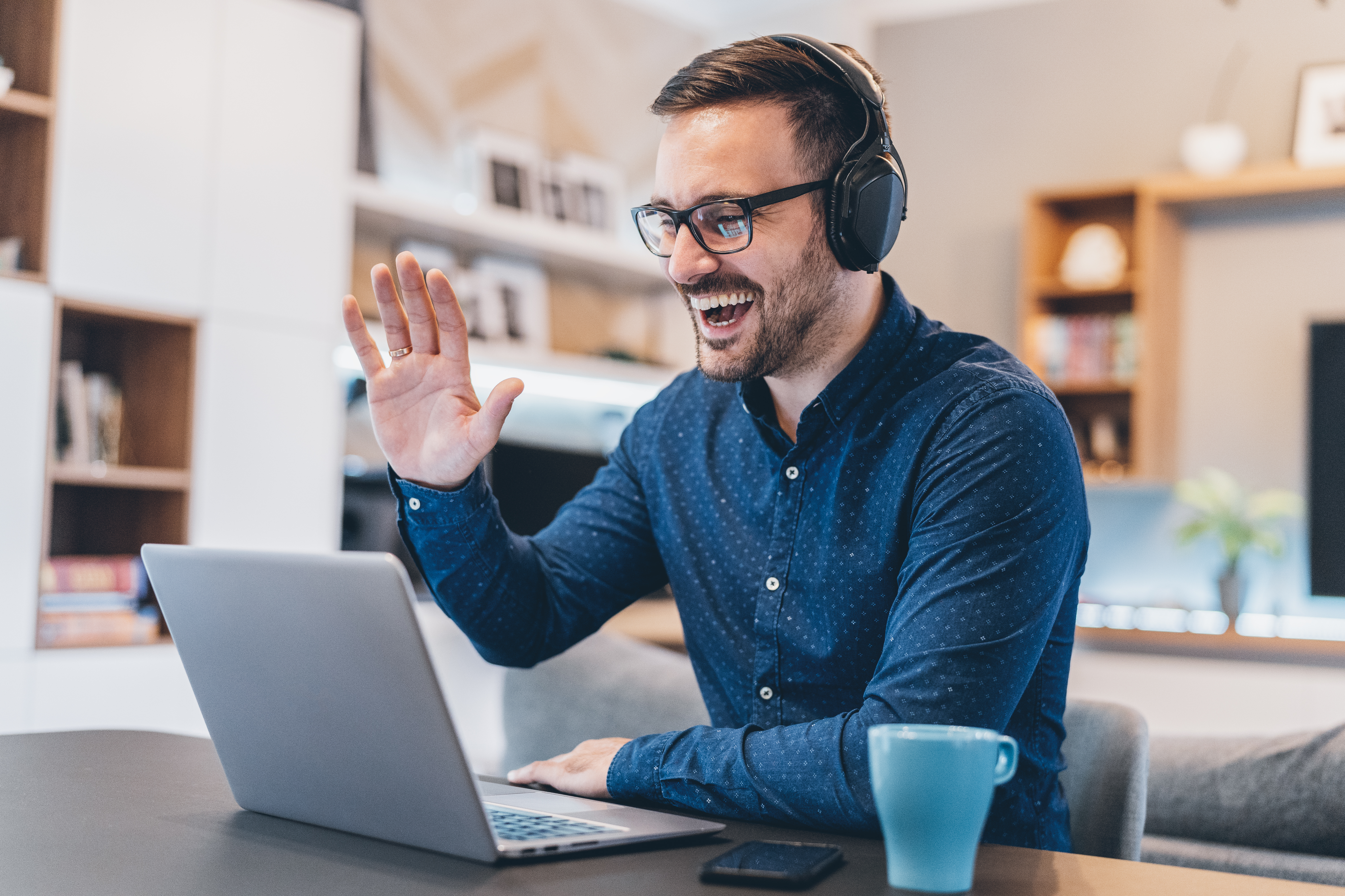 Man in headphones waving at laptop screen