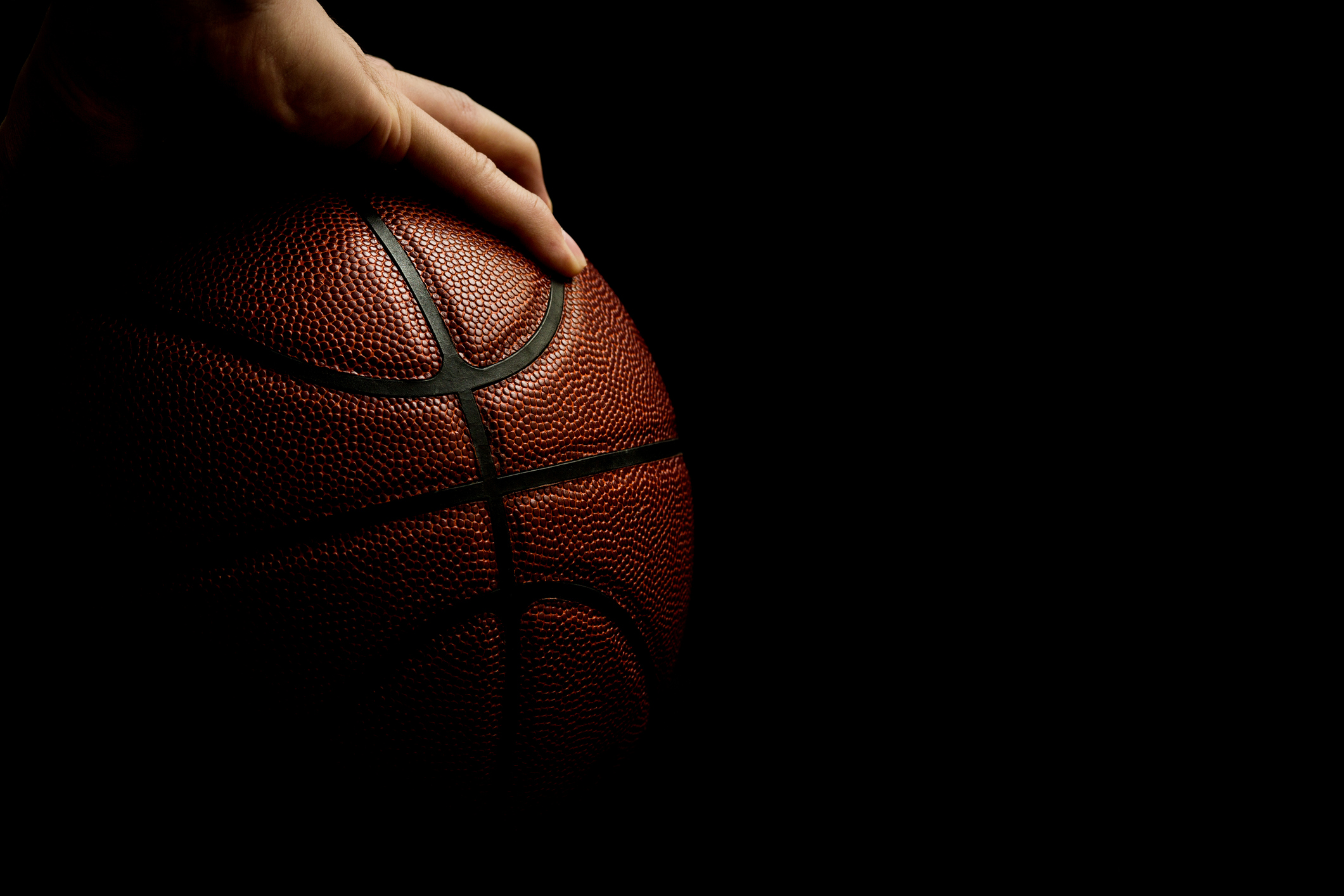 A hand holding a basketball against a black background.