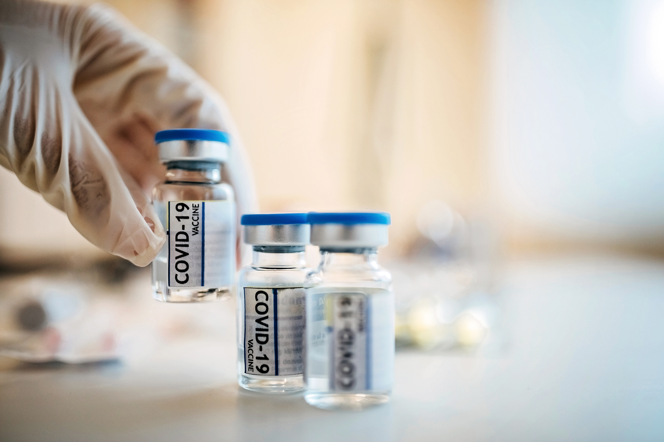 A researcher's hand sets a vial of coronavirus vaccine down on a counter next to two others.