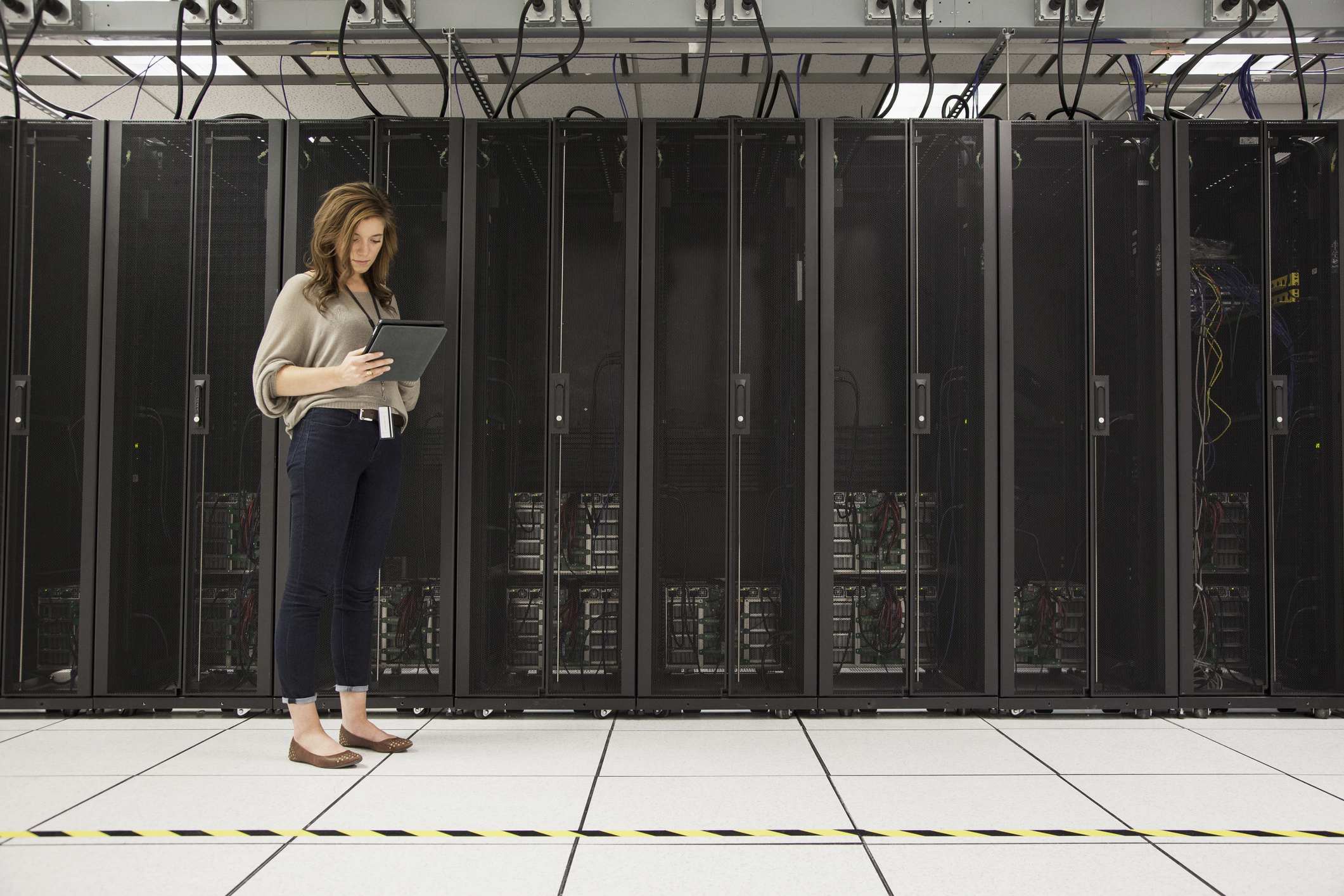 A woman holding a tablet standing in a server room.
