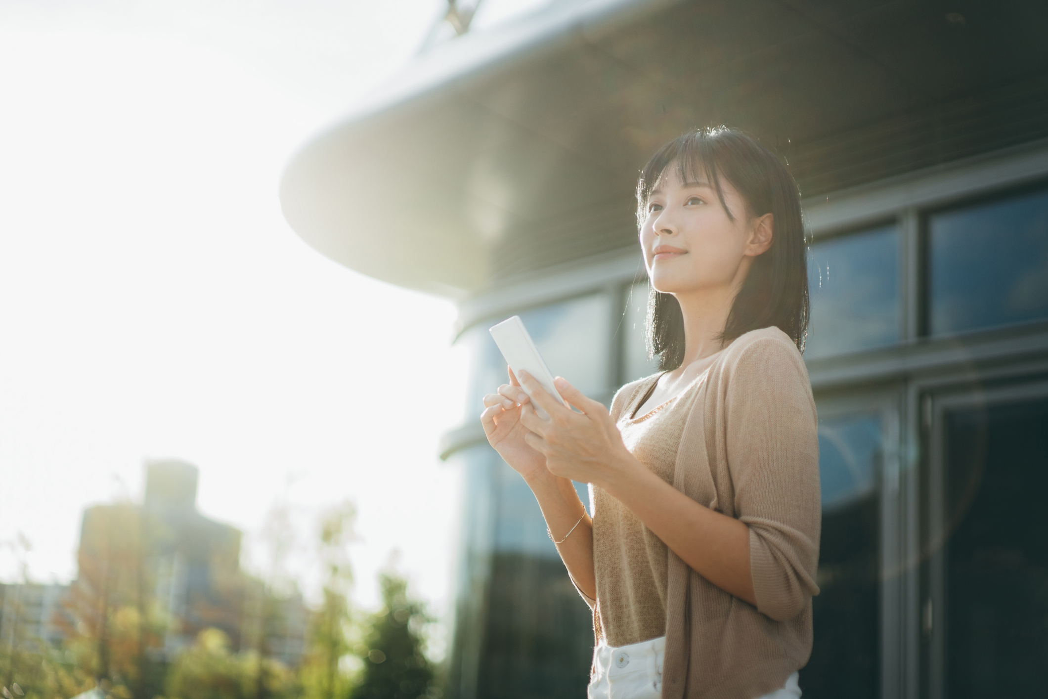 Happy young woman standing outdoors with mobile phone in hand.