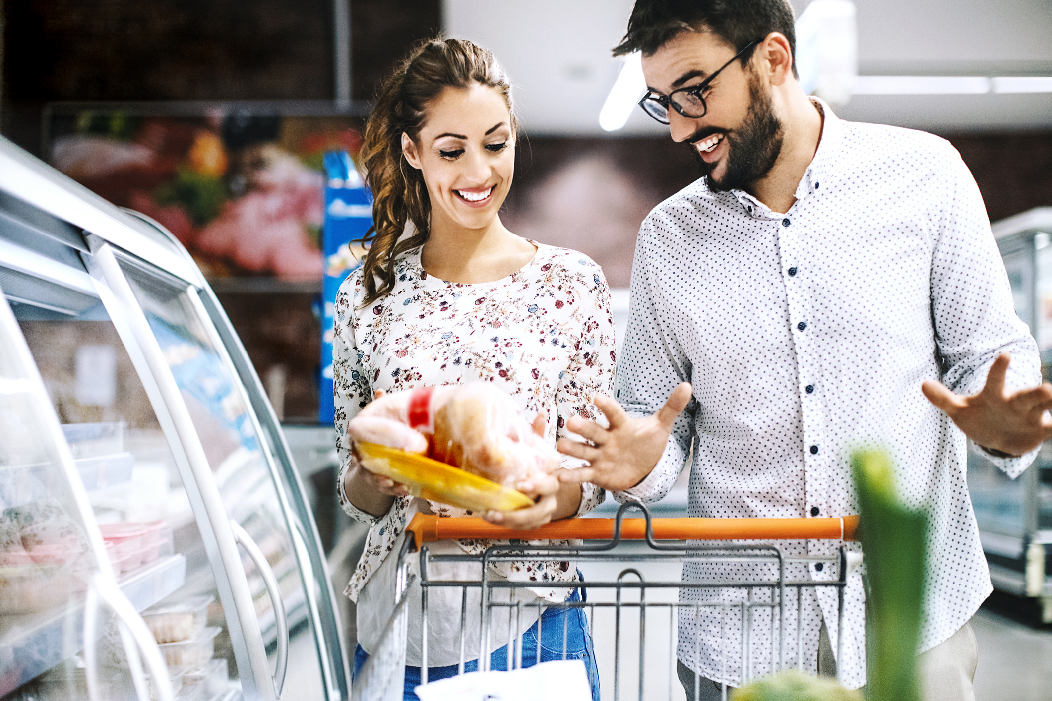 A couple looking at a frozen chicken in a supermarket.