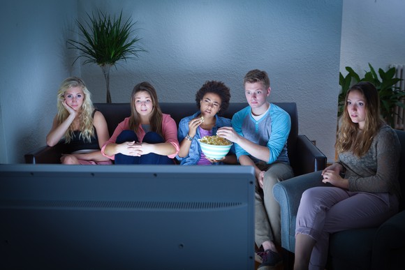 Group of teenagers watching TV while eating popcorn.