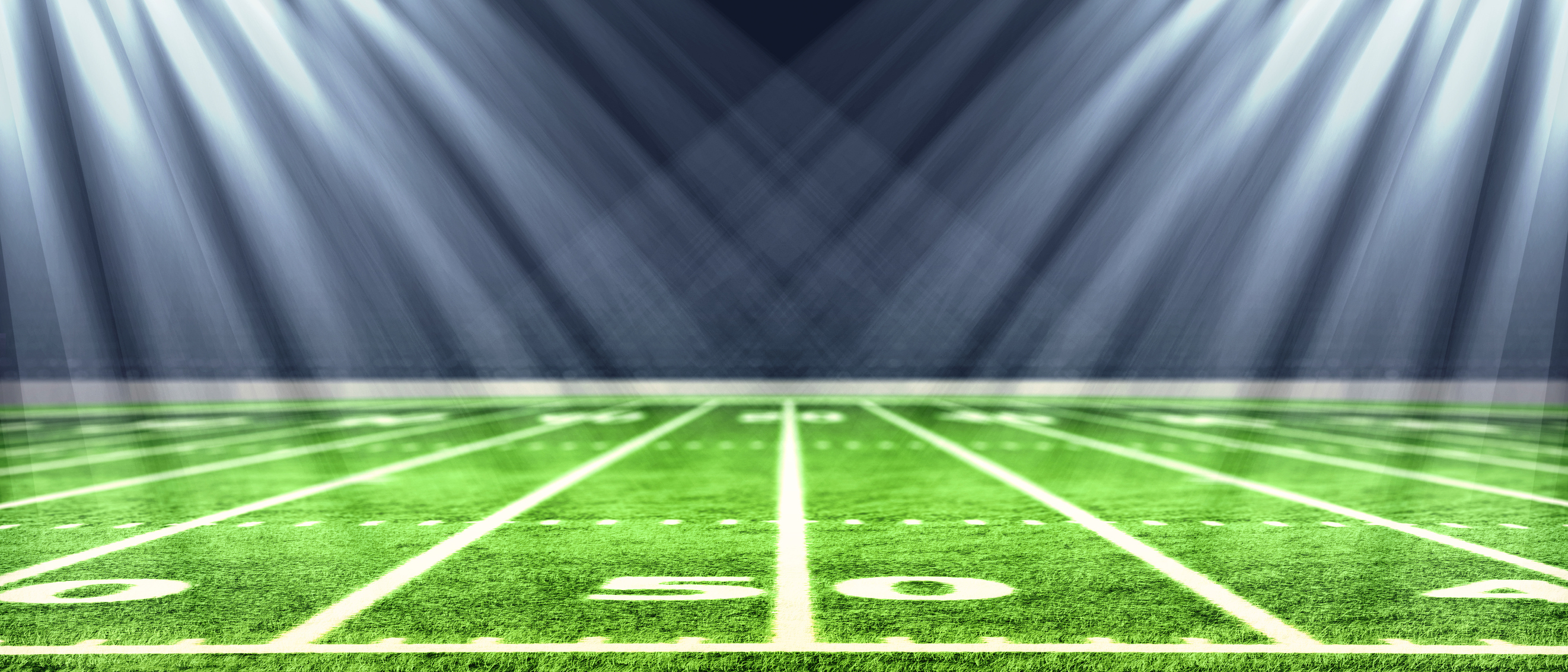 Lights are shining on the 50-yard line of a football field.