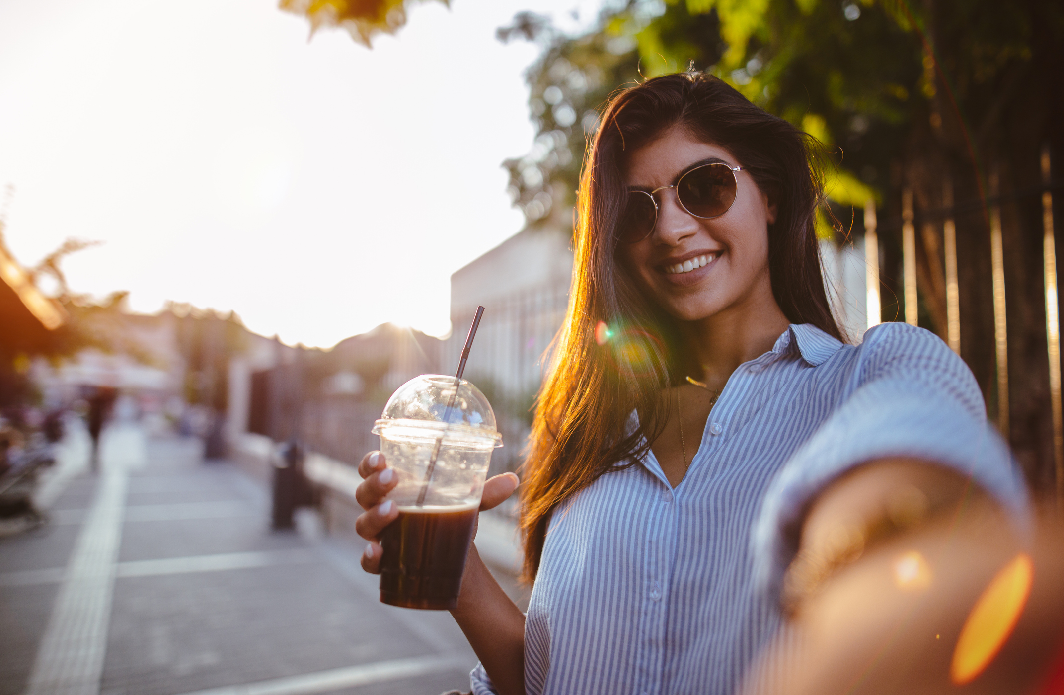 A young woman is holding a plastic coffee cup and smiling.