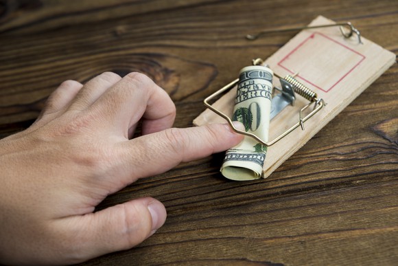 A person gets a finger stuck in a mouse trap while trying to grab a bill.