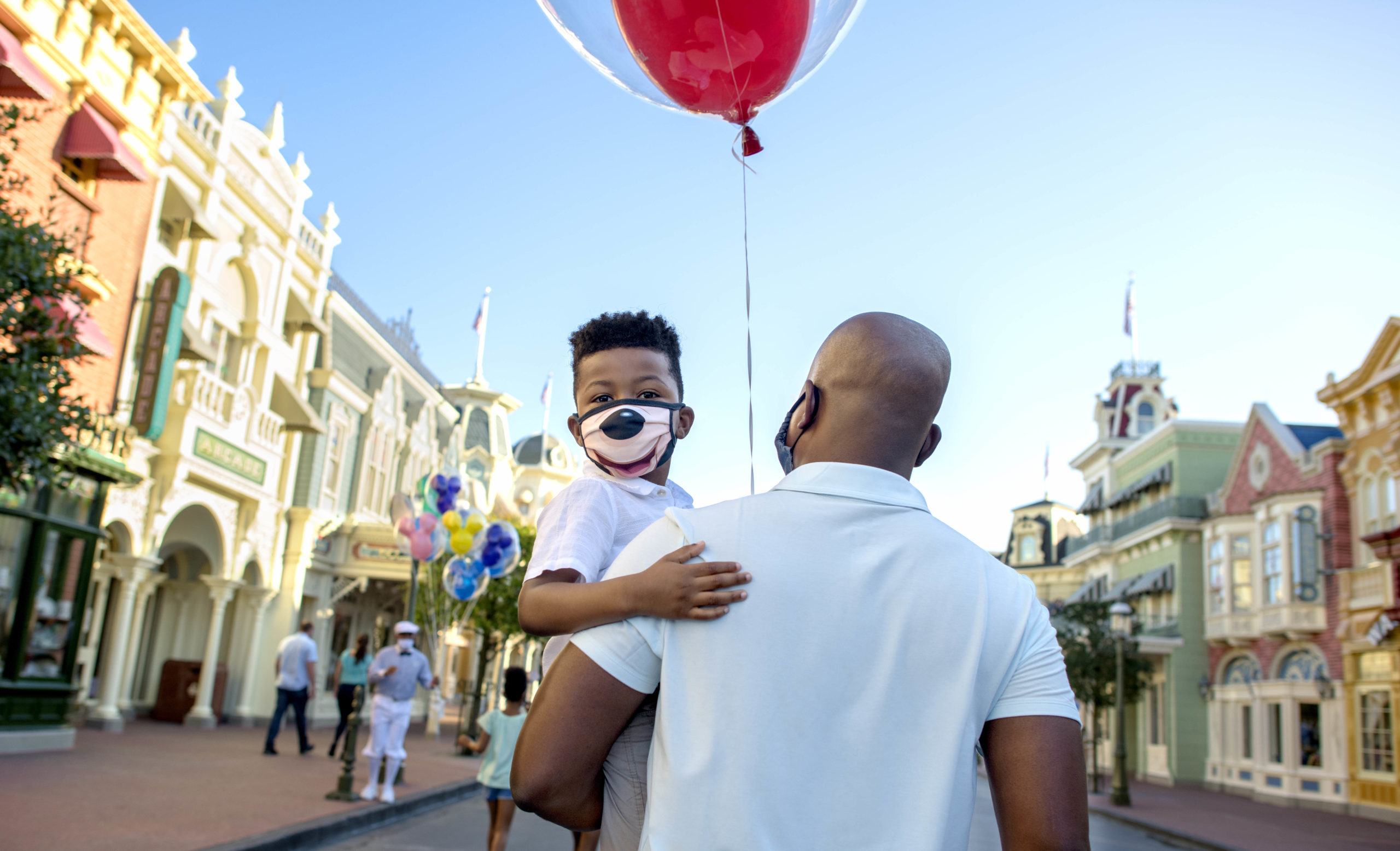 A dad holds his masked son as the walk in Disneyland.