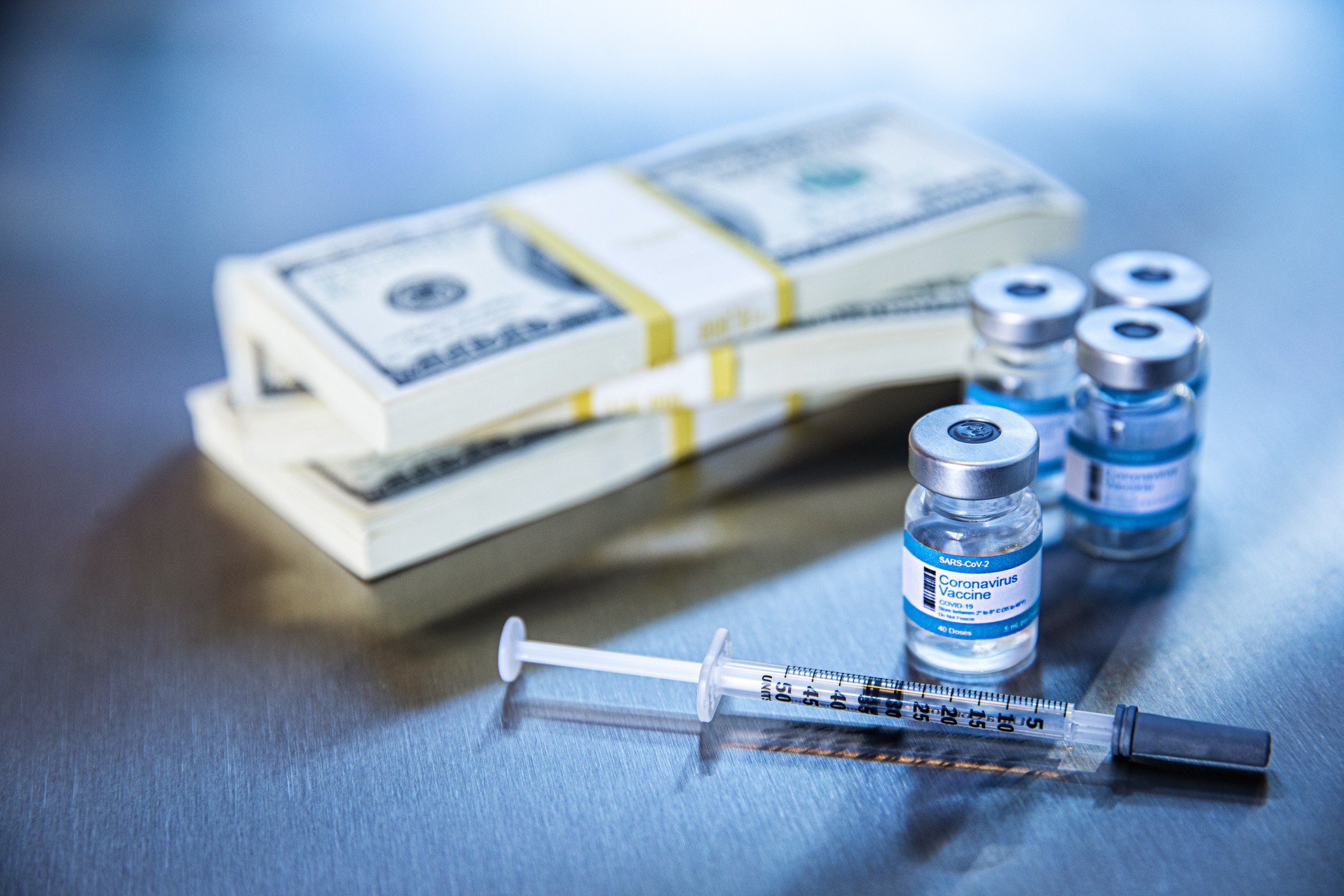 Vaccine vials and a syringe next to stacks of cash