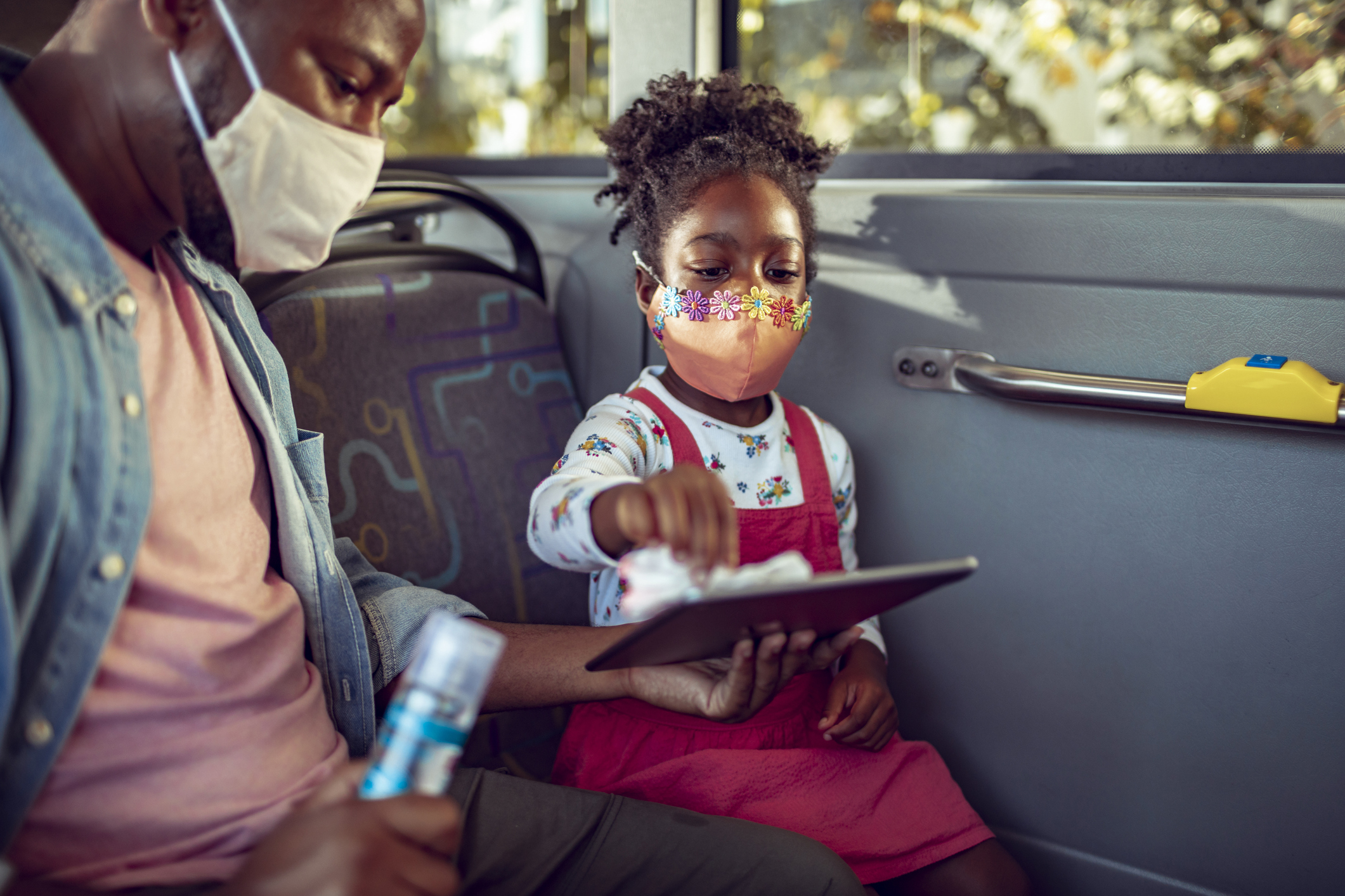 A man holds a tablet as his daughter cleans it with a wipe.