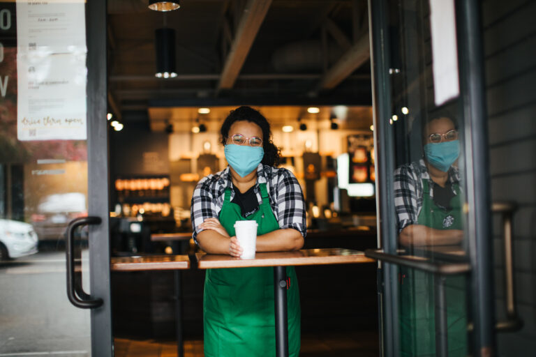 A Starbucks barista wearing a mask and serving coffee.