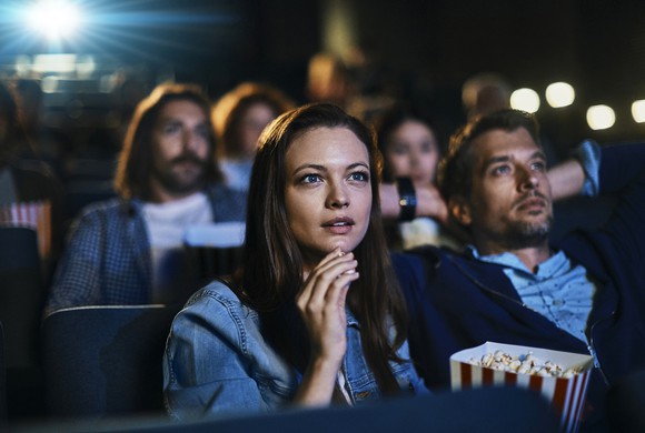 A couple eating popcorn while watching a film in a crowded theater. 