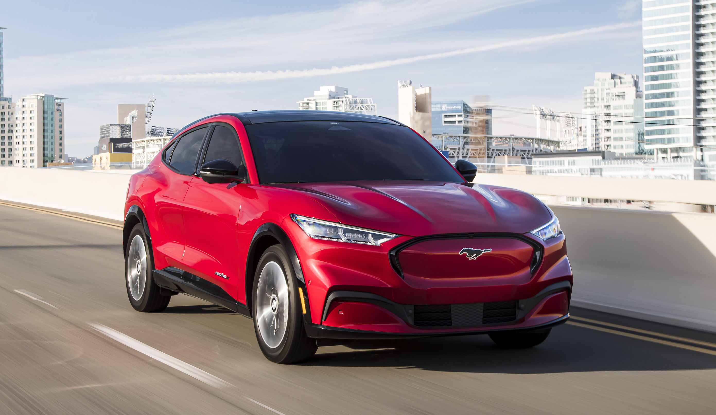 A red Ford Mustang Mach-E, a sporty electric crossover, on a highway.