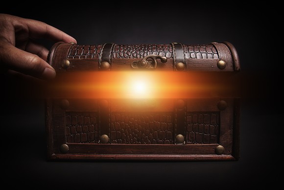 A hand opens a small treasure chest that's glowing on the inside.