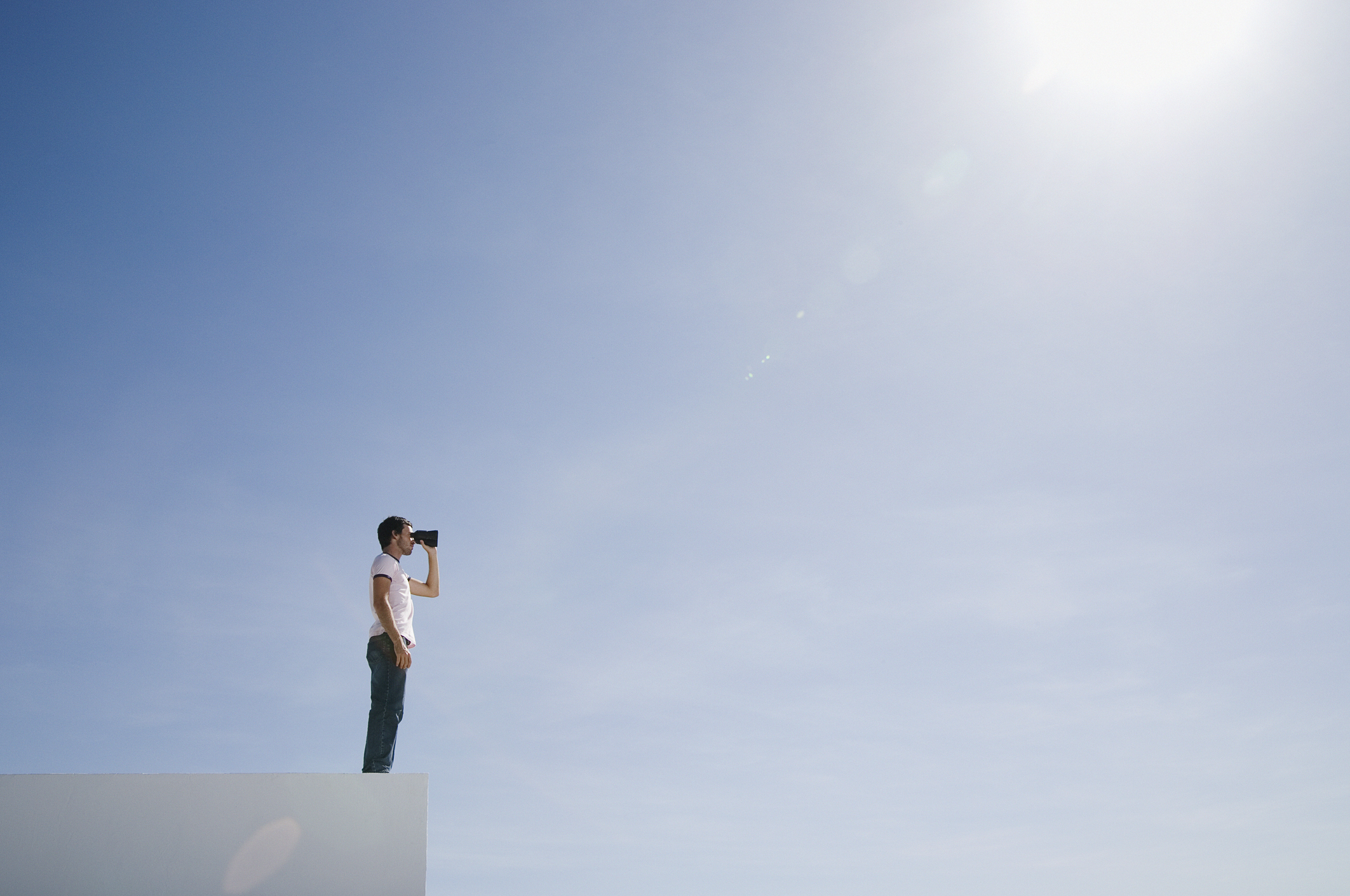 Man looking through binoculars under sunny blue skies.