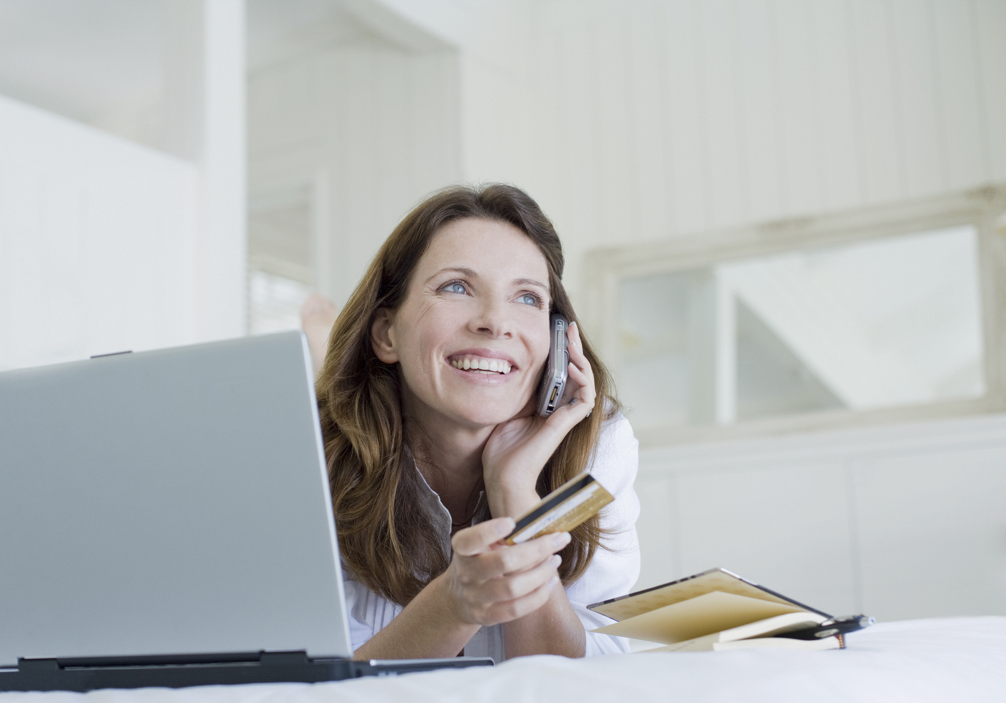 Woman on computer and phone while holding credit card