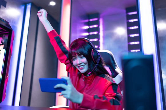 A young woman pumping her fist in the air while holding a mobile phone during an Esports tournament. 